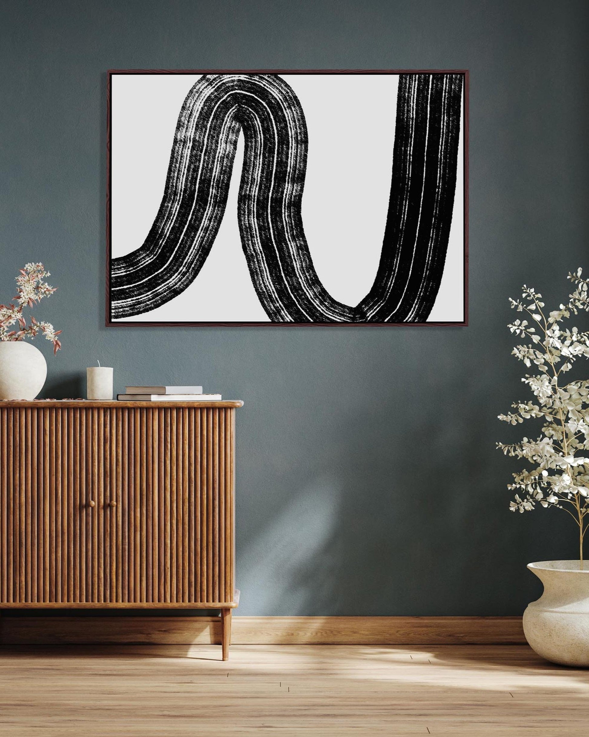 Abstract black and white artwork on a gray wall above a wooden cabinet.