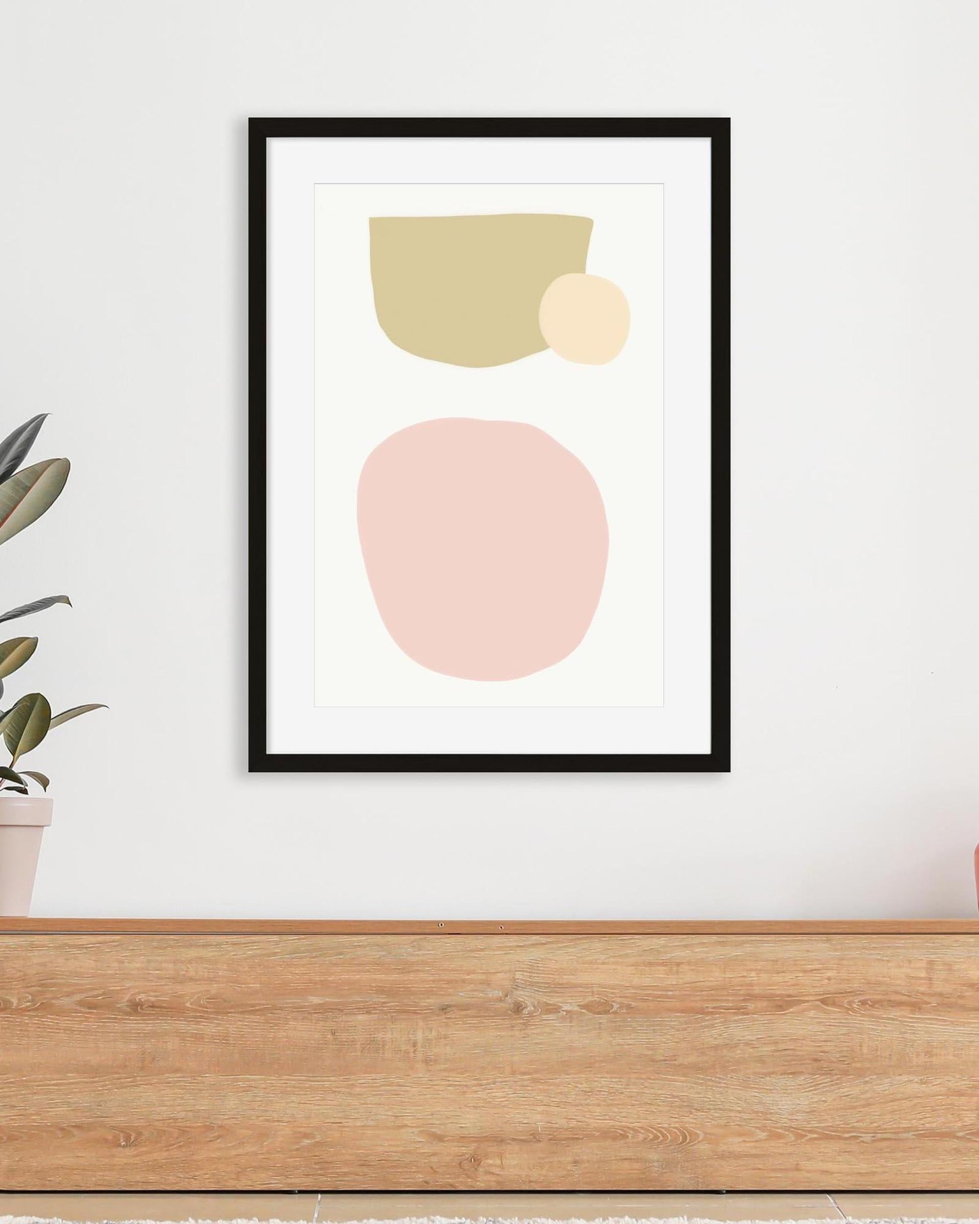 Framed abstract art print with geometric shapes on a white wall above a wooden surface.