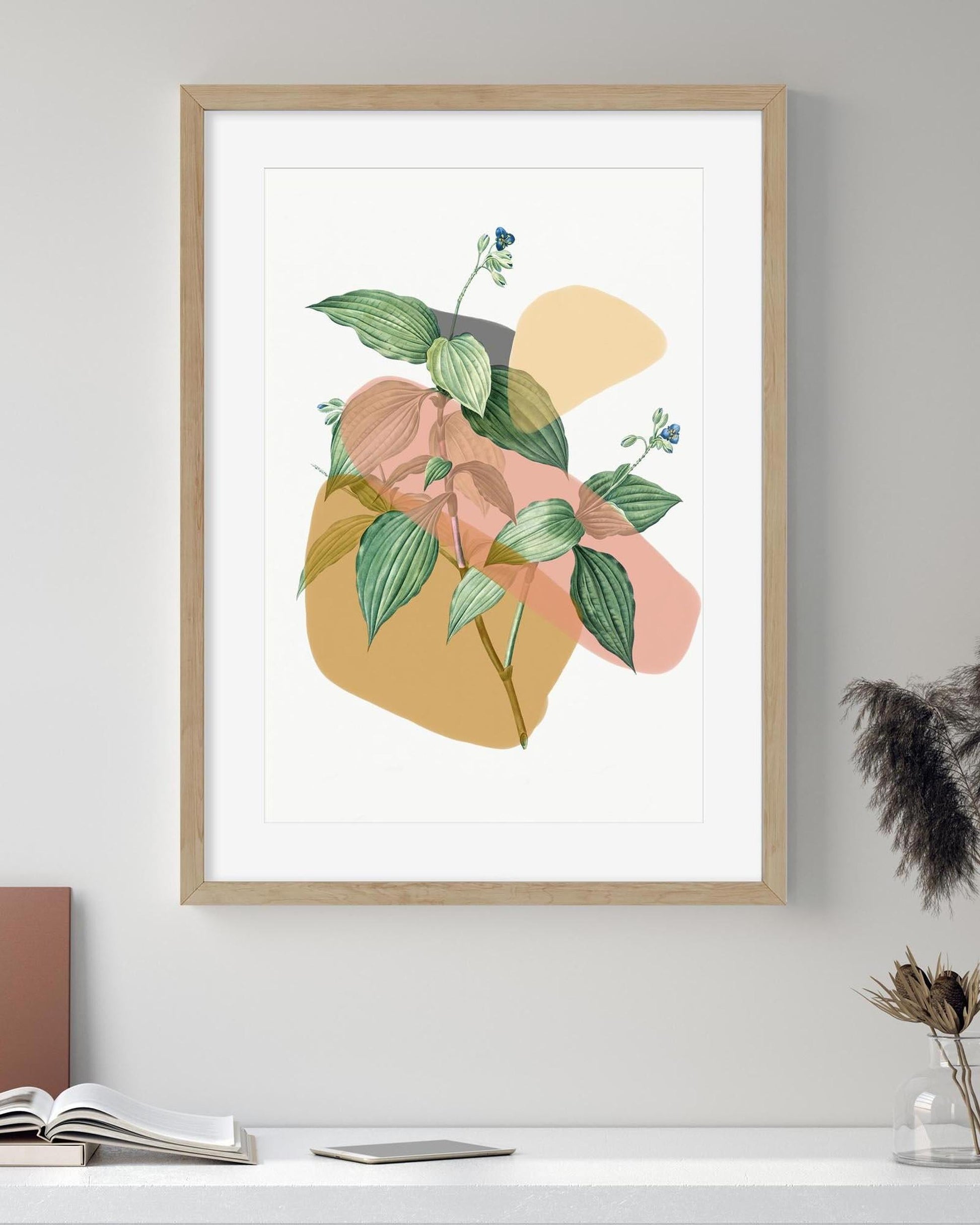 Framed abstract art print with colorful leaves on a white wall.