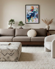 Modern living room with a gray sofa, patterned ottoman, and colorful abstract painting on the wall.