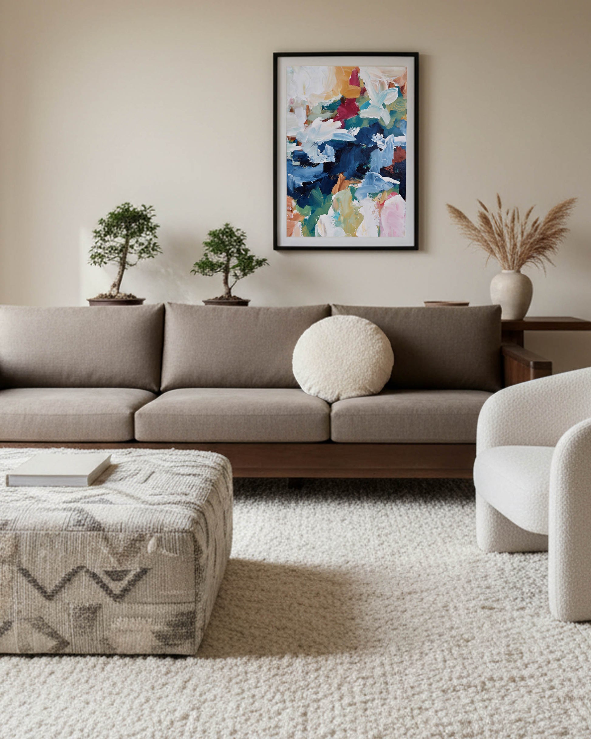 Modern living room with a gray sofa, patterned ottoman, and colorful abstract painting on the wall.