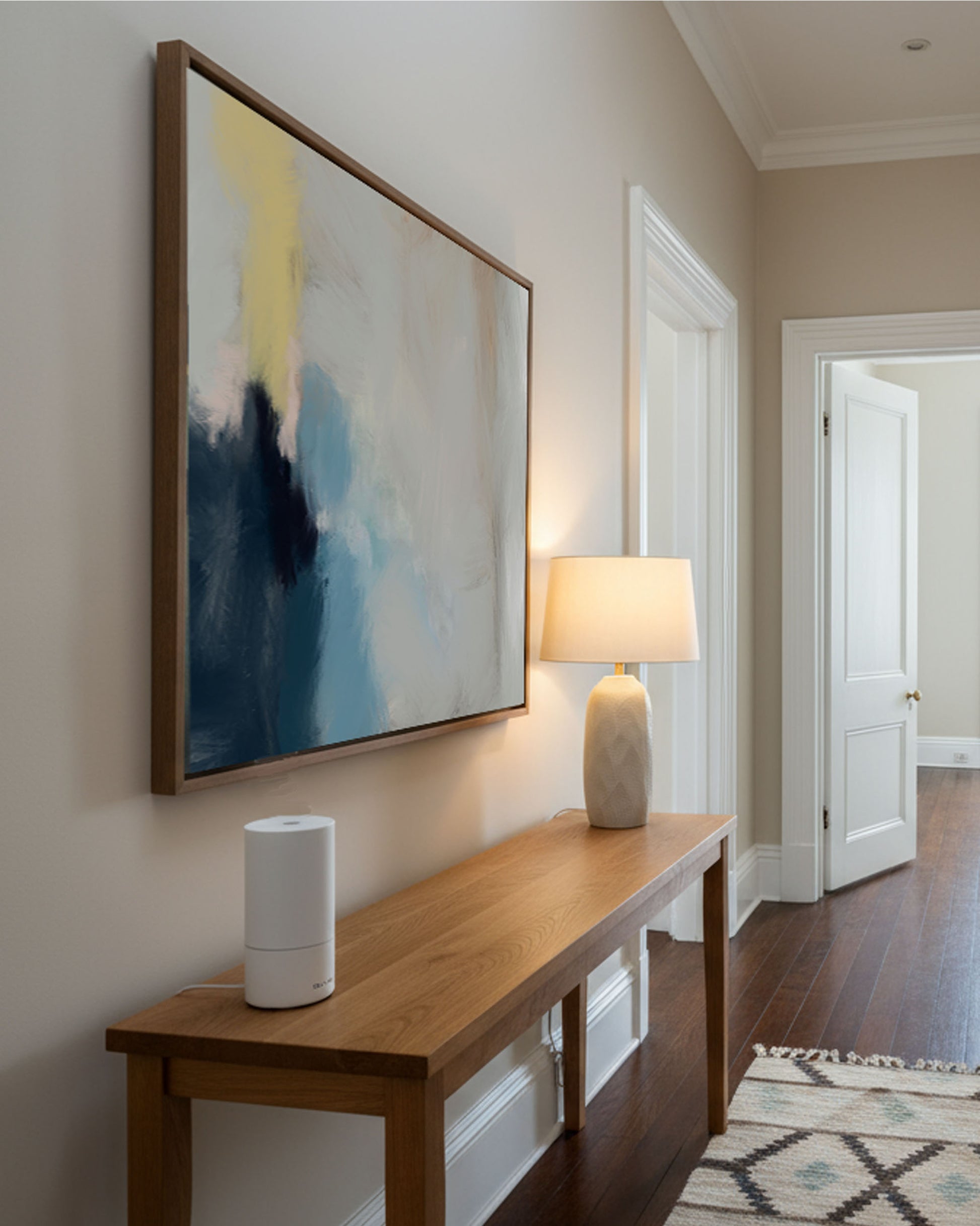 Modern abstract wall art print on canvas, blue modern art, minimal entrance hallway with oak side table and beige lamp, natural wooden floors.