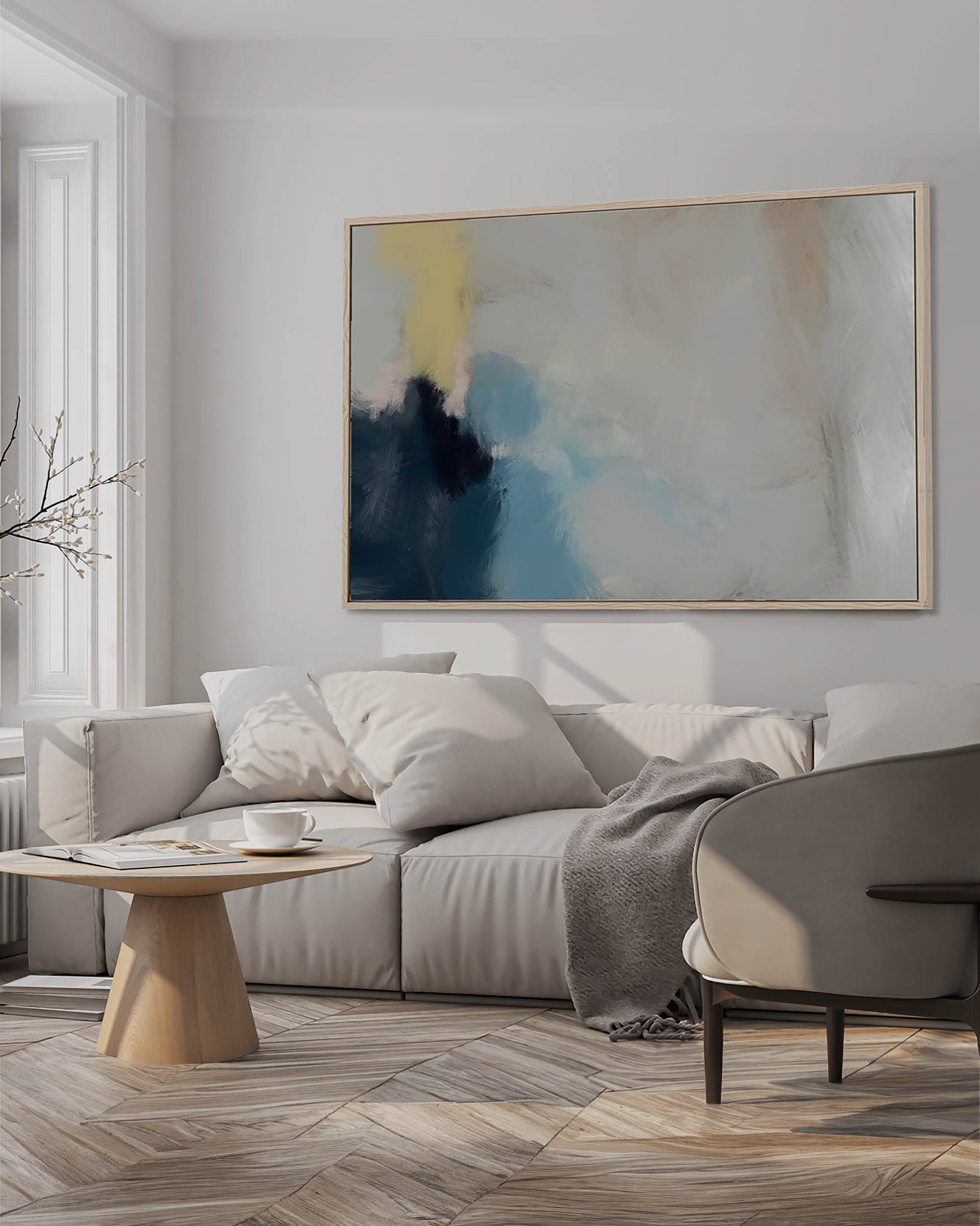 A framed canvas abstract art piece with neutral greys and whites displayed above a gray sofa in a well-lit living room.