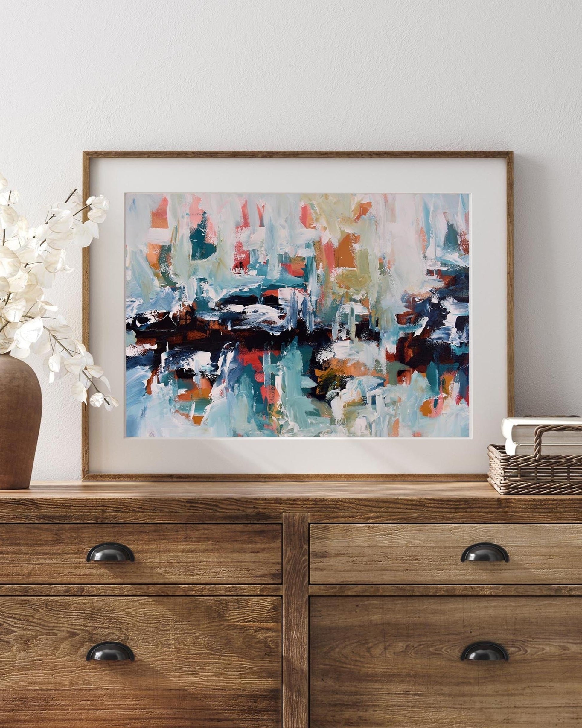 Framed abstract painting on a wooden dresser with decorative items.