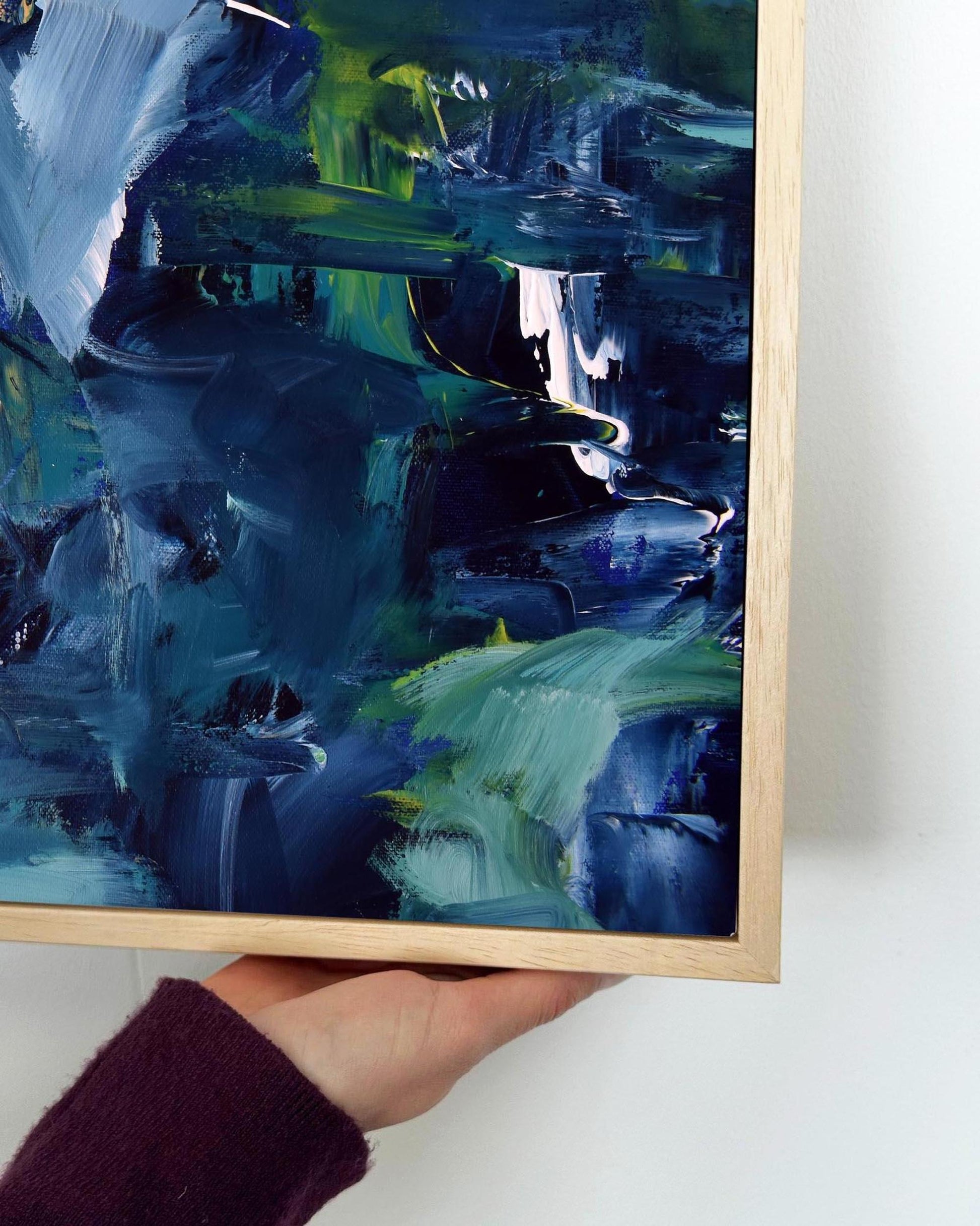 Abstract painting with blue and green hues held by a person against a white background