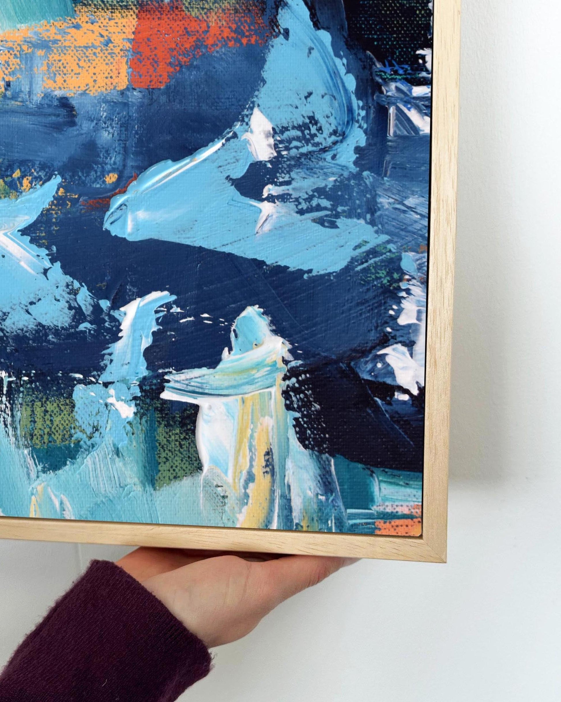 Abstract painting with blue and orange tones held by a hand on a white surface