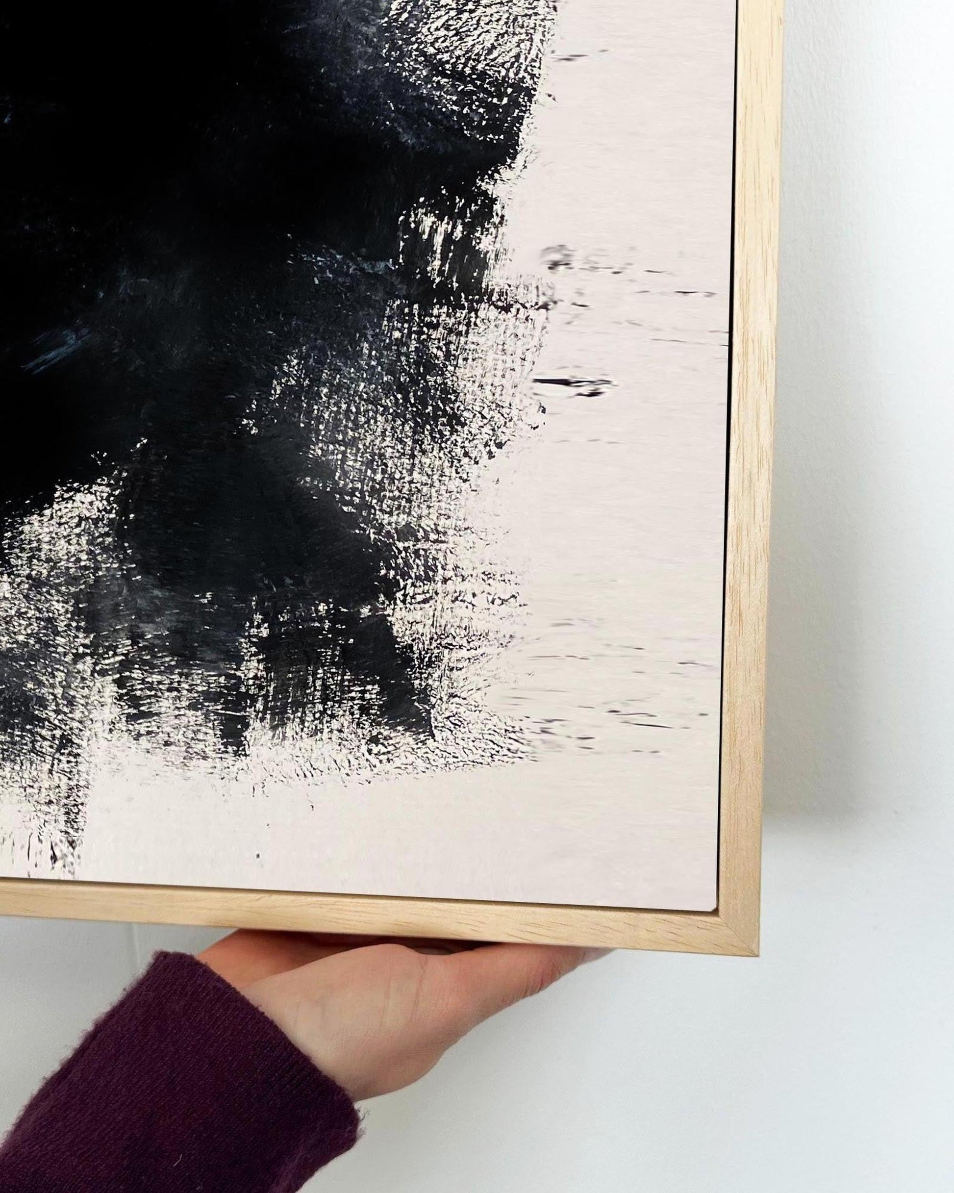 Abstract painting with black and white brush strokes in a wooden frame held by a person.