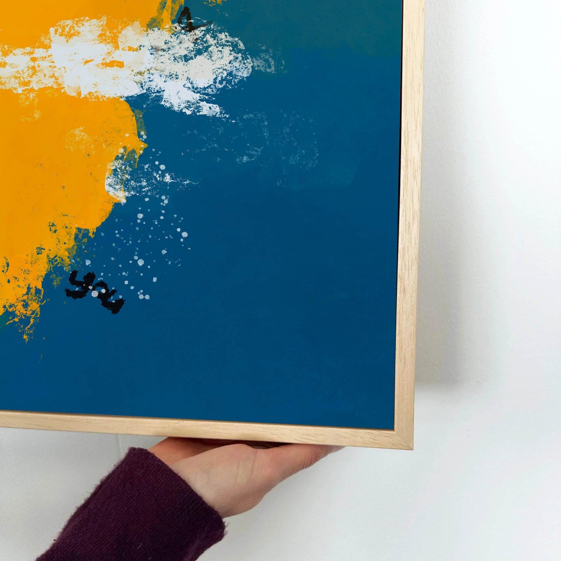 Framed abstract art with blue background and orange splash held by a hand.