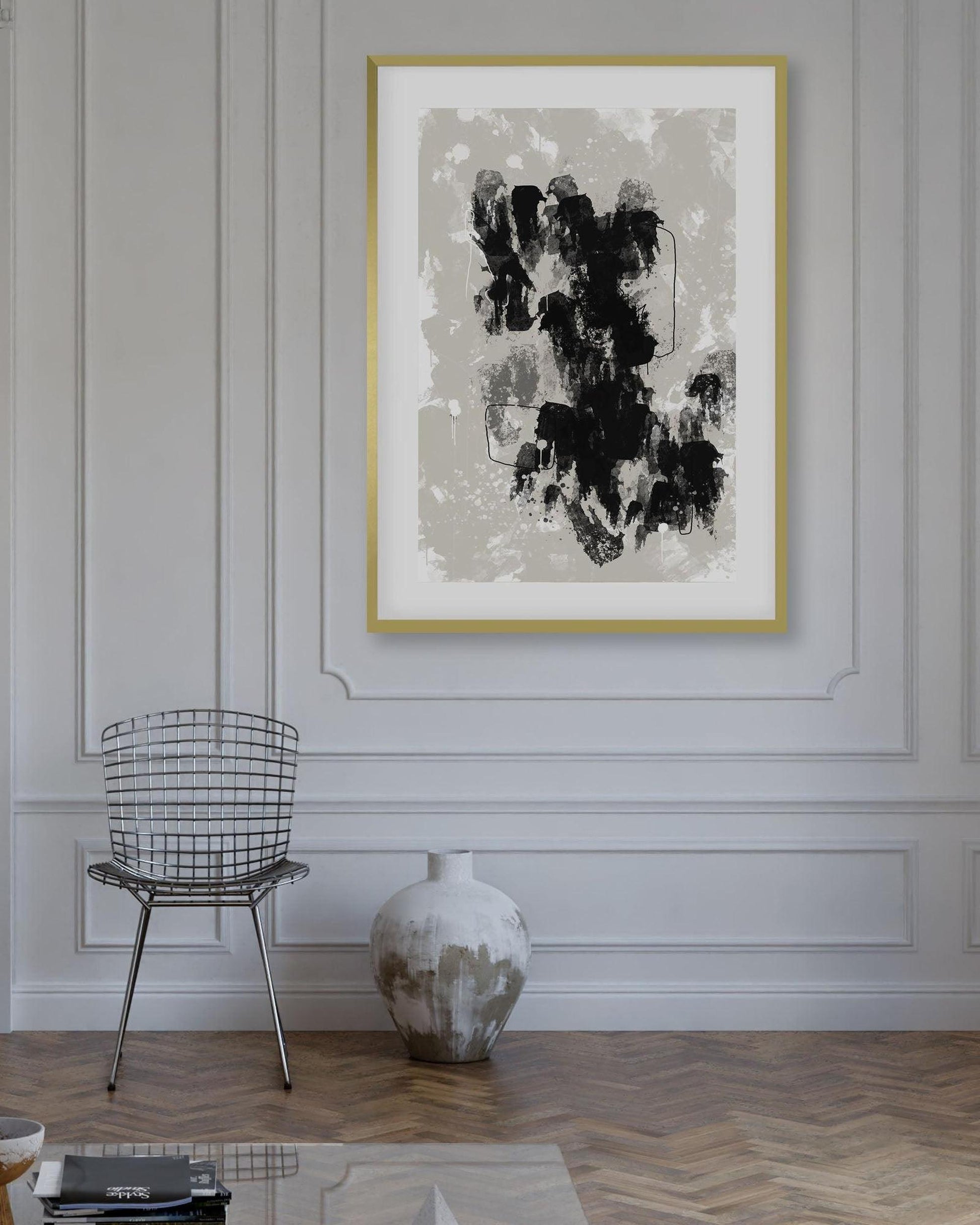 Abstract art print in a gold frame on a wall above a chair and vase.