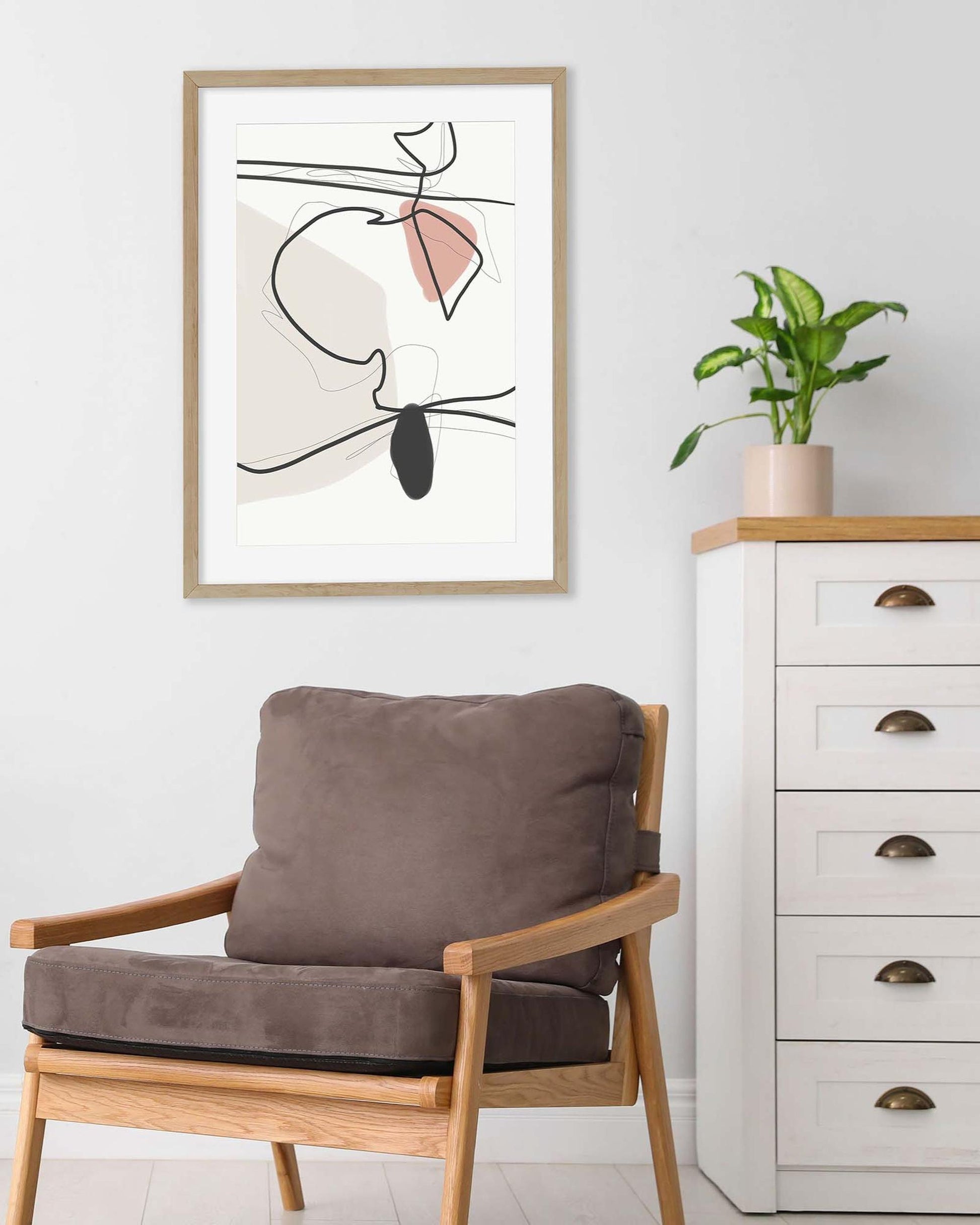 Modern interior with a wooden armchair, abstract art, and a white dresser.