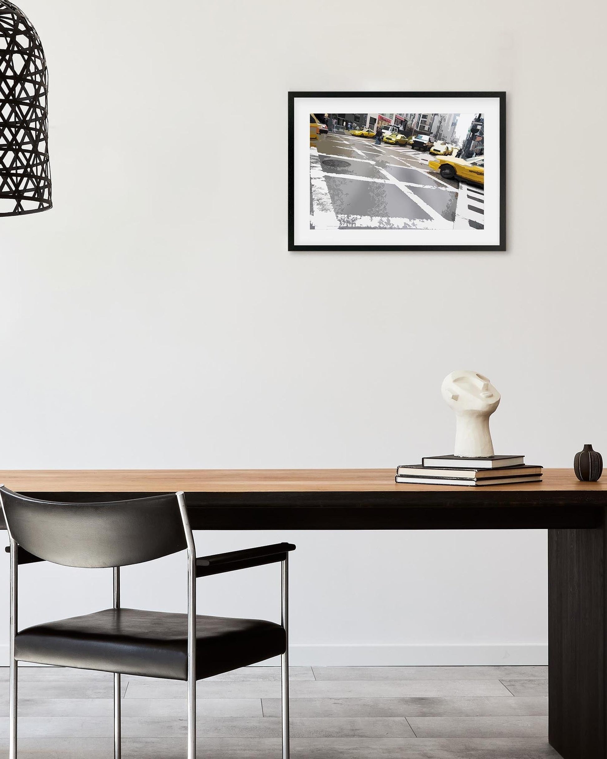 Framed artwork above a wooden desk with a chair in a room setting.