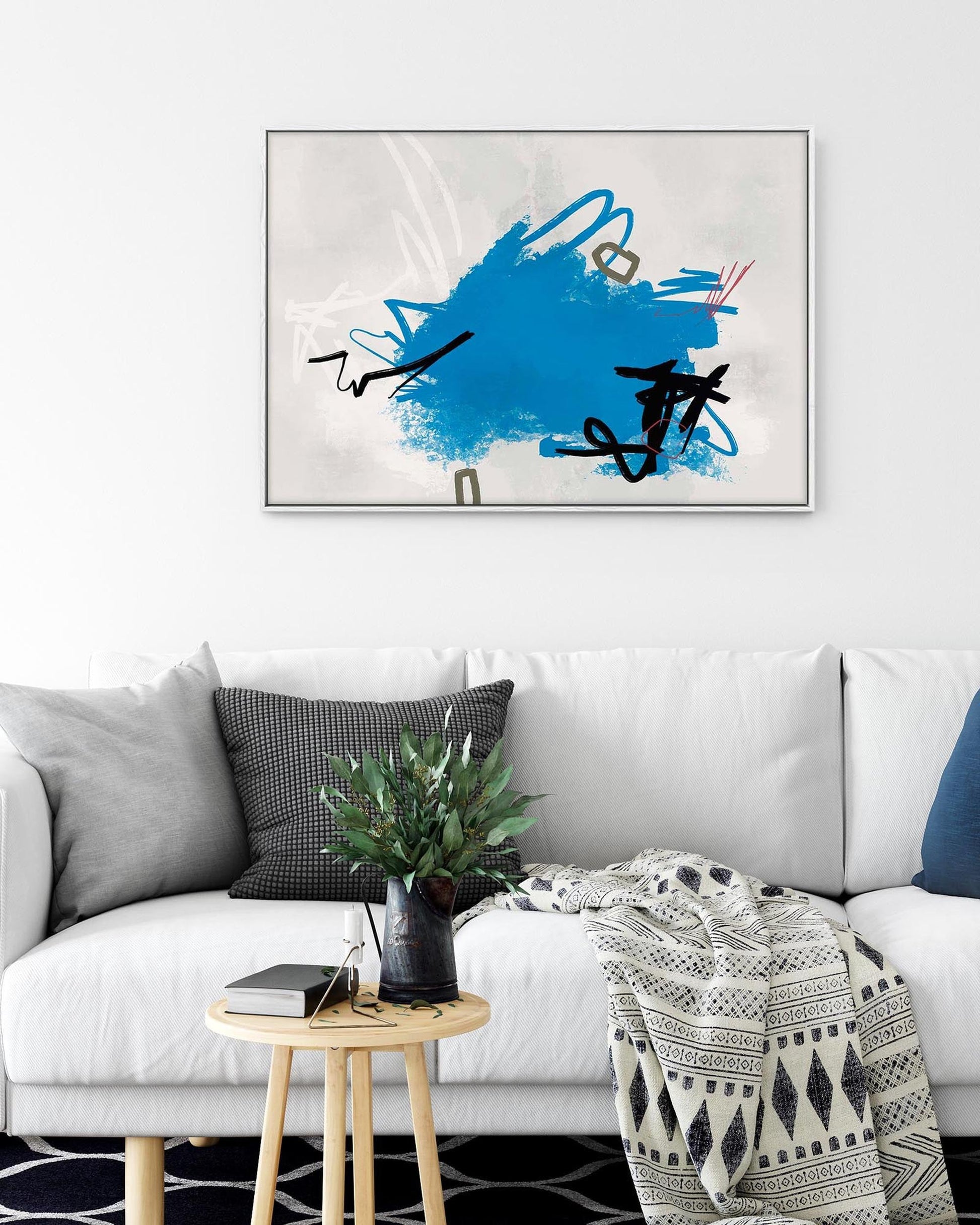 Living room with a white sofa, abstract art on the wall, and a small table with a plant.