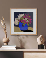 Framed artwork of flowers in a blue vase on a wall above a shelf with decorative items.