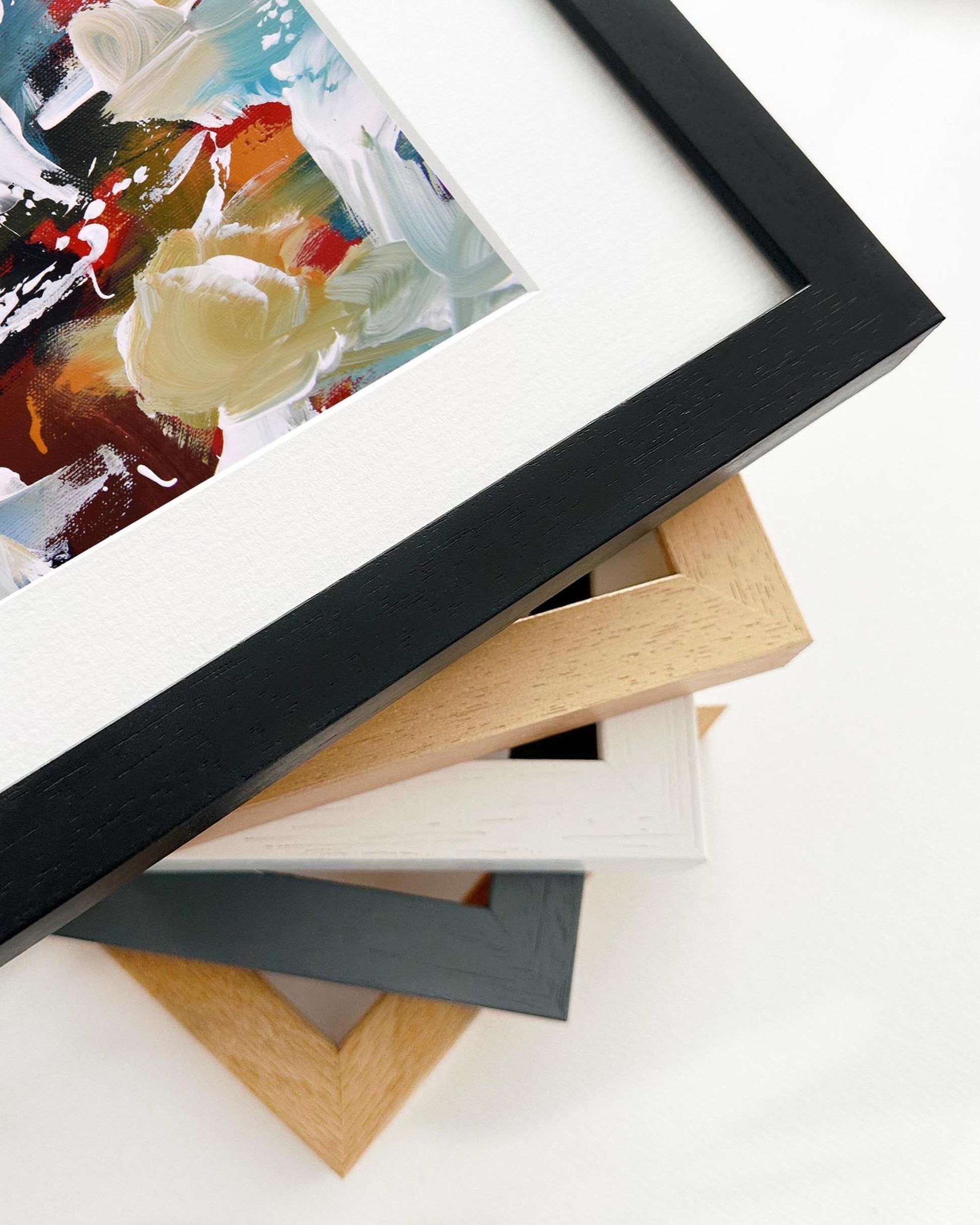 Stack of variously colored picture frames on a white surface with a partially visible abstract painting.
