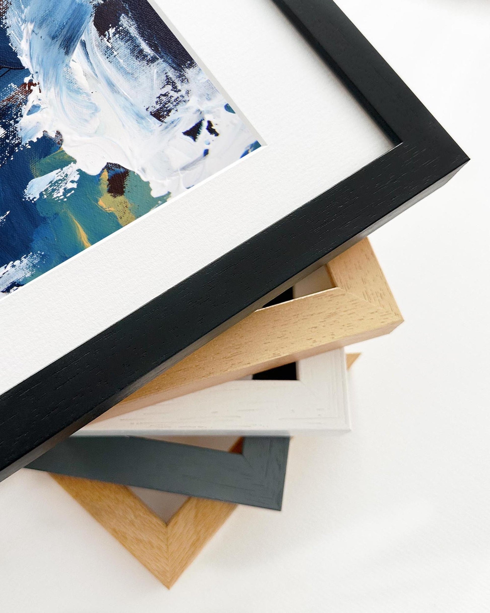 Stack of picture frames with a partially visible framed artwork on a white background