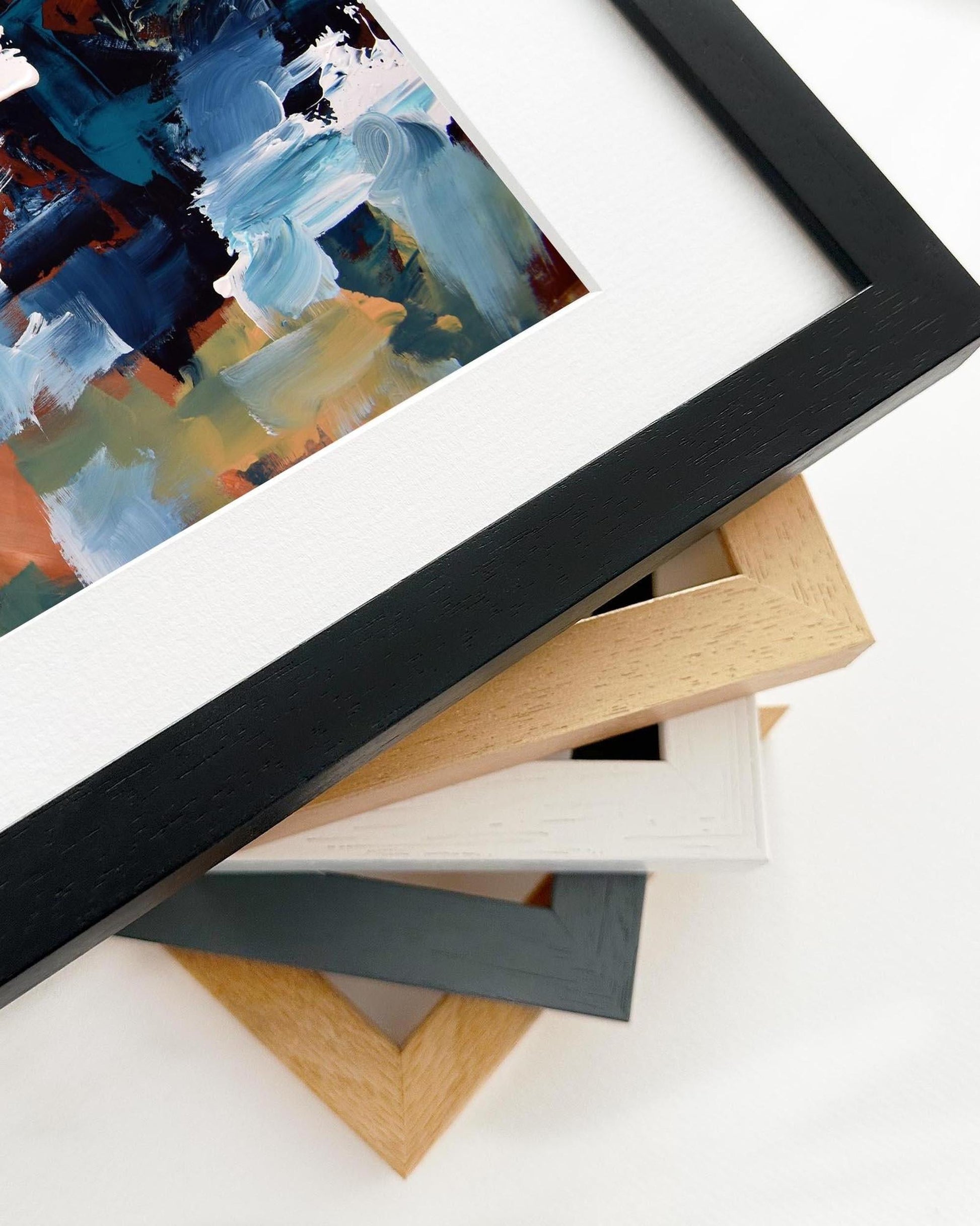 Collection of variously colored picture frames on a white surface with a partially visible abstract painting.