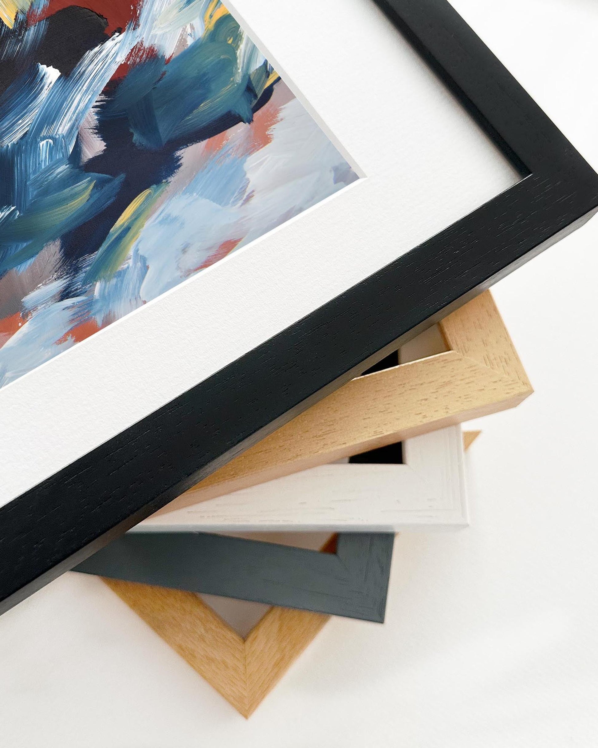 Close-up of various picture frames on a white surface with a colorful abstract painting in the background.