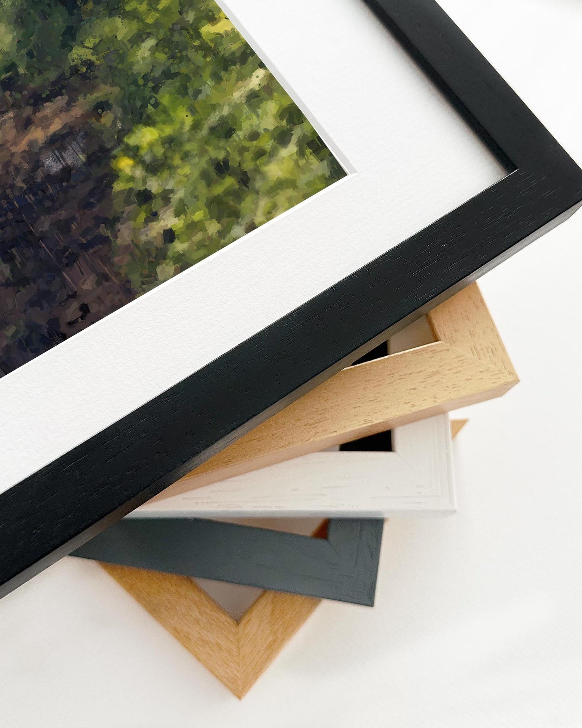 Close-up of various picture frames on a white surface with a blurred painting in the background.