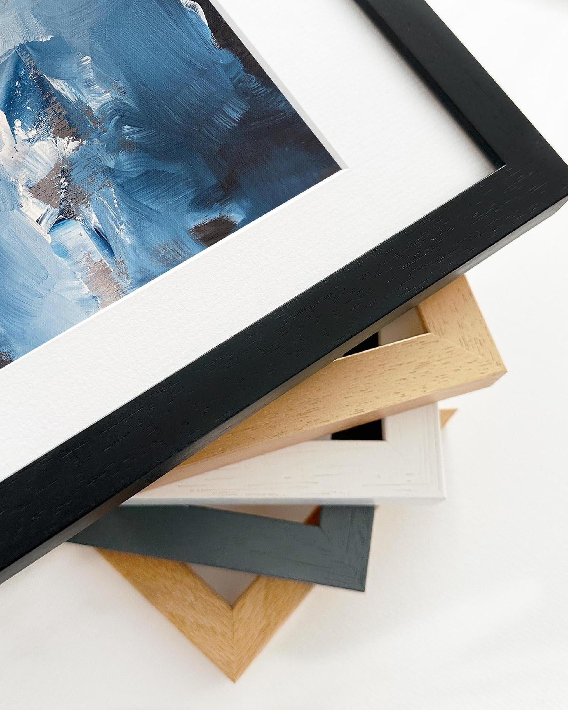 Collection of various picture frames on a white surface with a painting in the background.