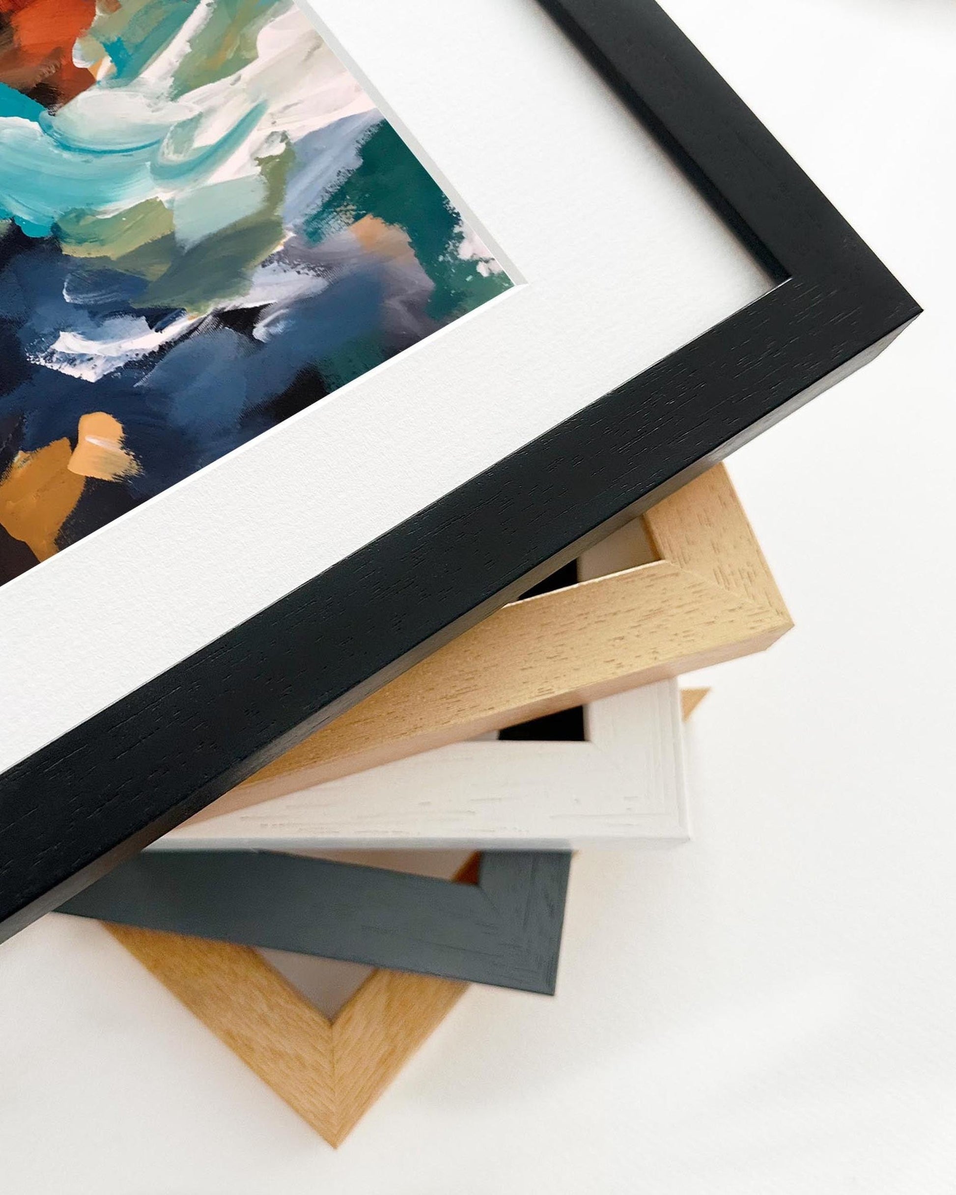 Stack of variously framed artworks on a white surface