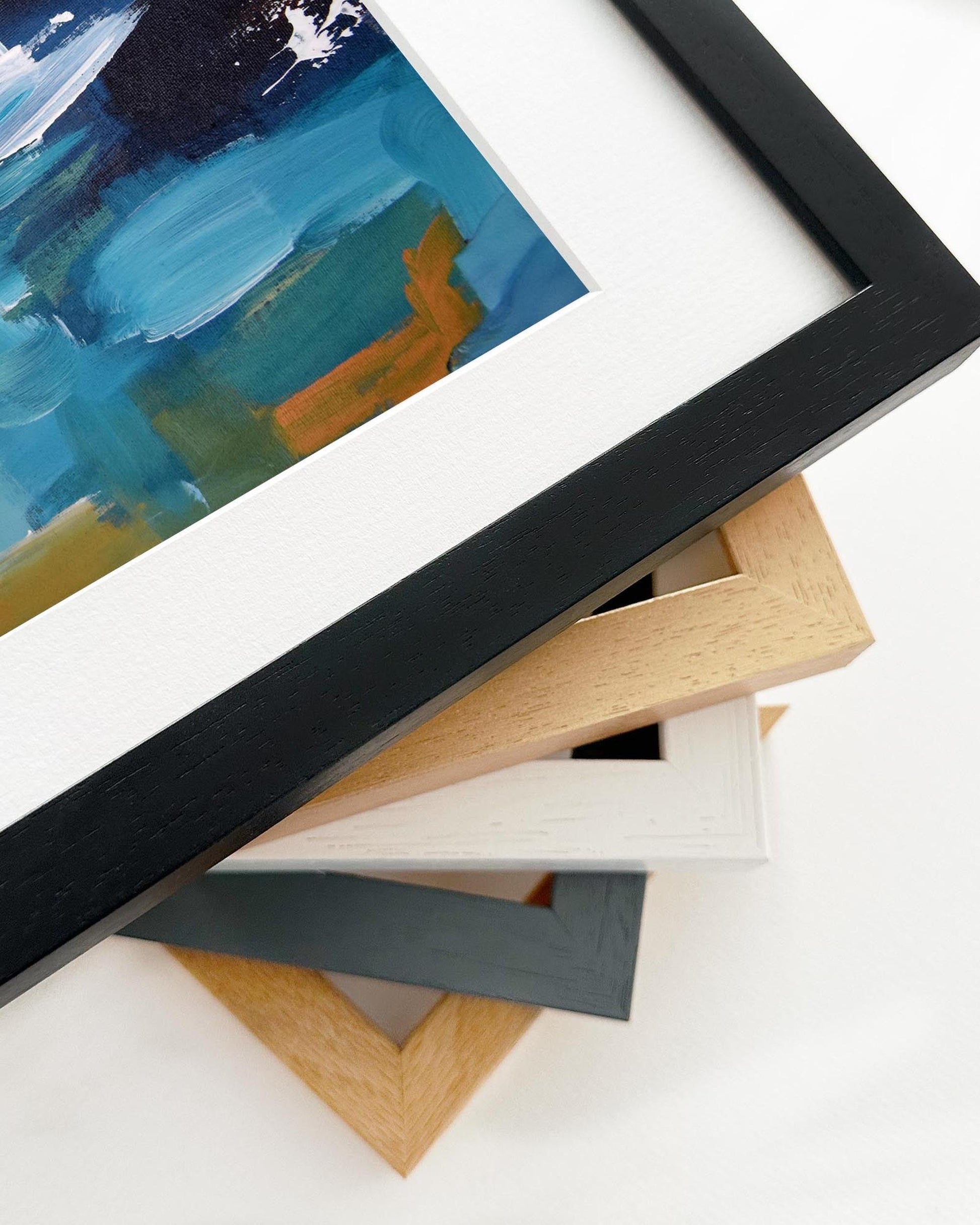 Stack of variously colored picture frames on a white surface with a partially visible abstract painting.