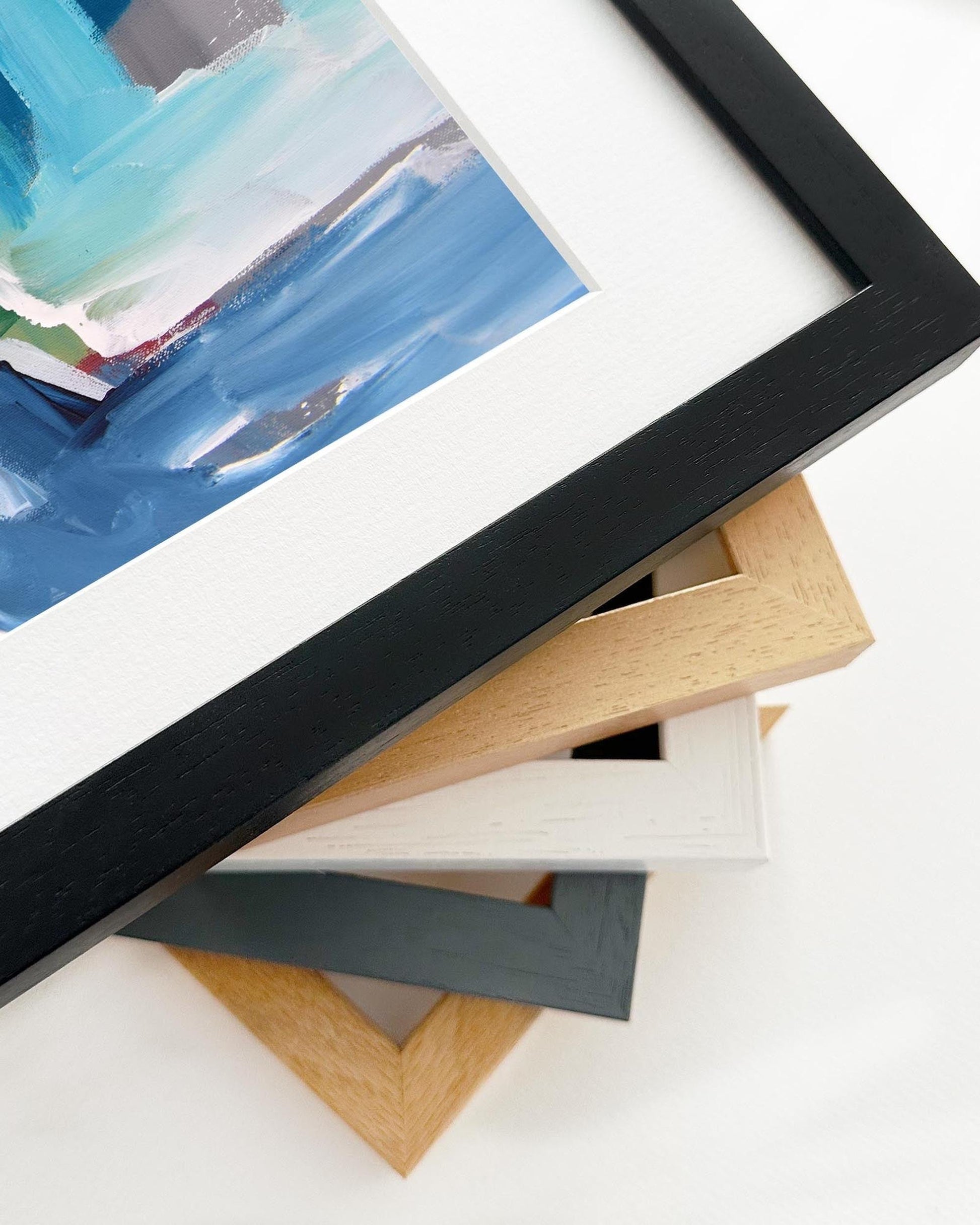 Close-up of various picture frames on a white surface with a partially visible painting.