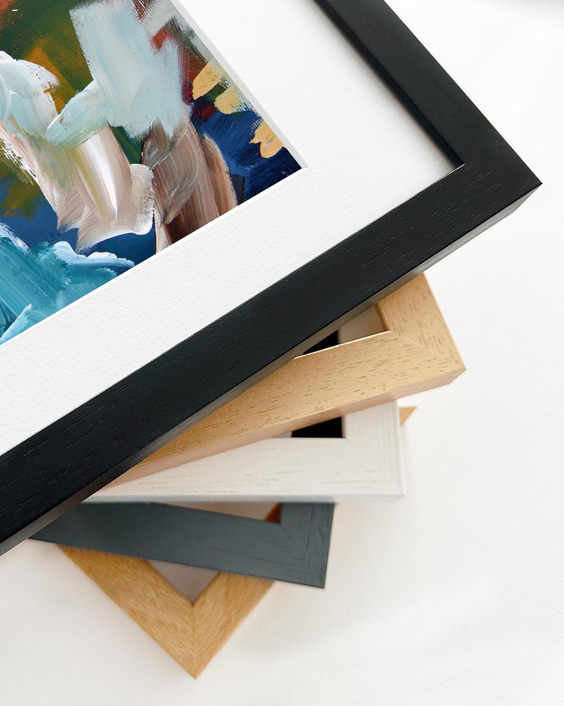 Stack of various picture frames on a white surface with a partially visible framed artwork.