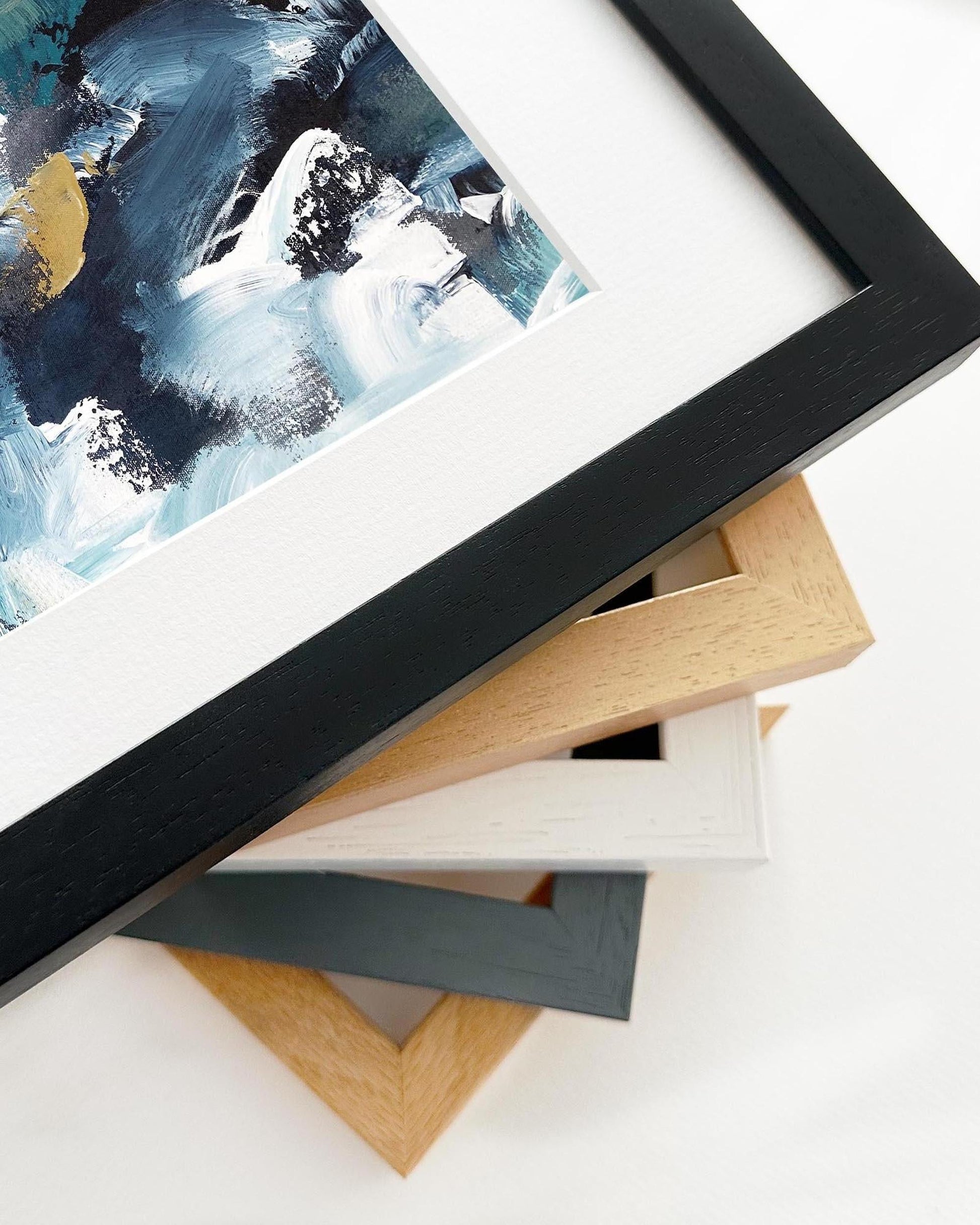 Framed abstract painting with a stack of variously colored frames on a white surface