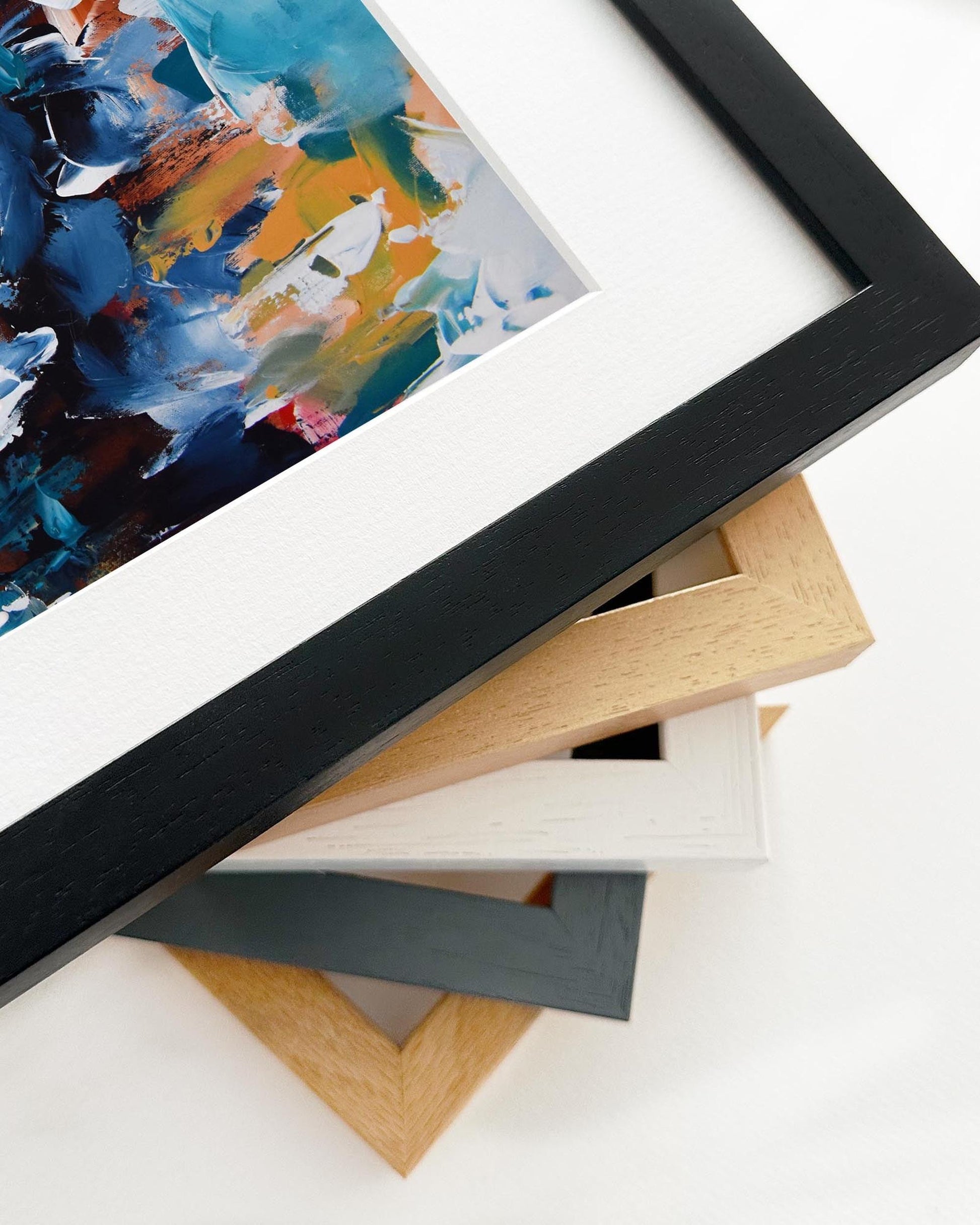 Stack of various picture frames with a partially visible abstract painting in the background.