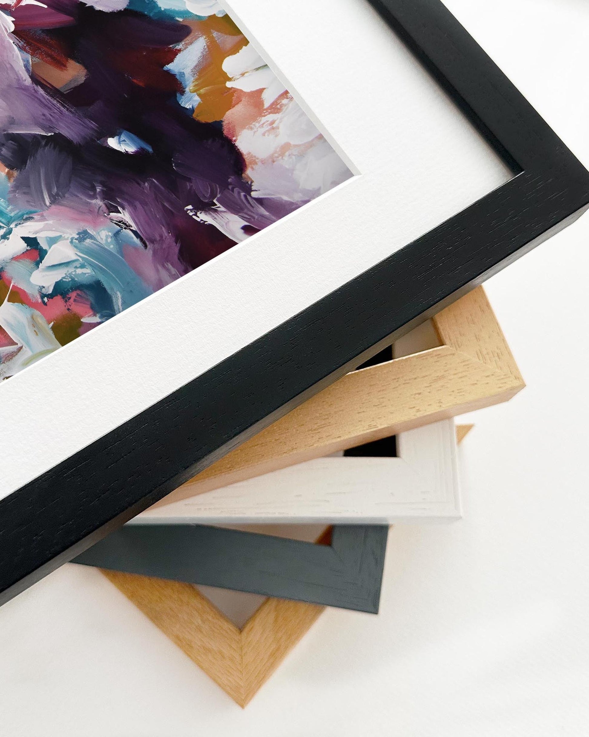 Close-up of various picture frames with a colorful abstract painting in the background.
