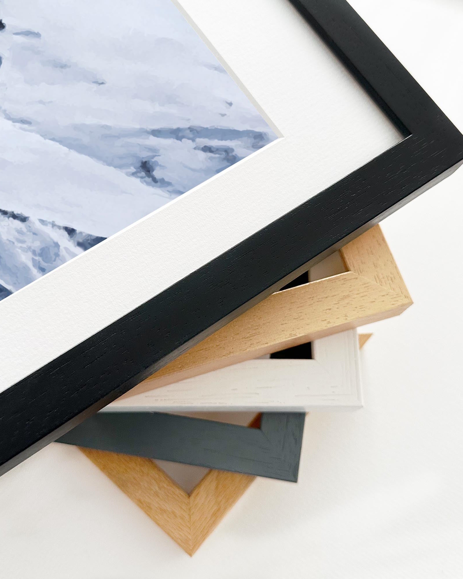 Stack of picture frames with a partially visible framed artwork on a white background