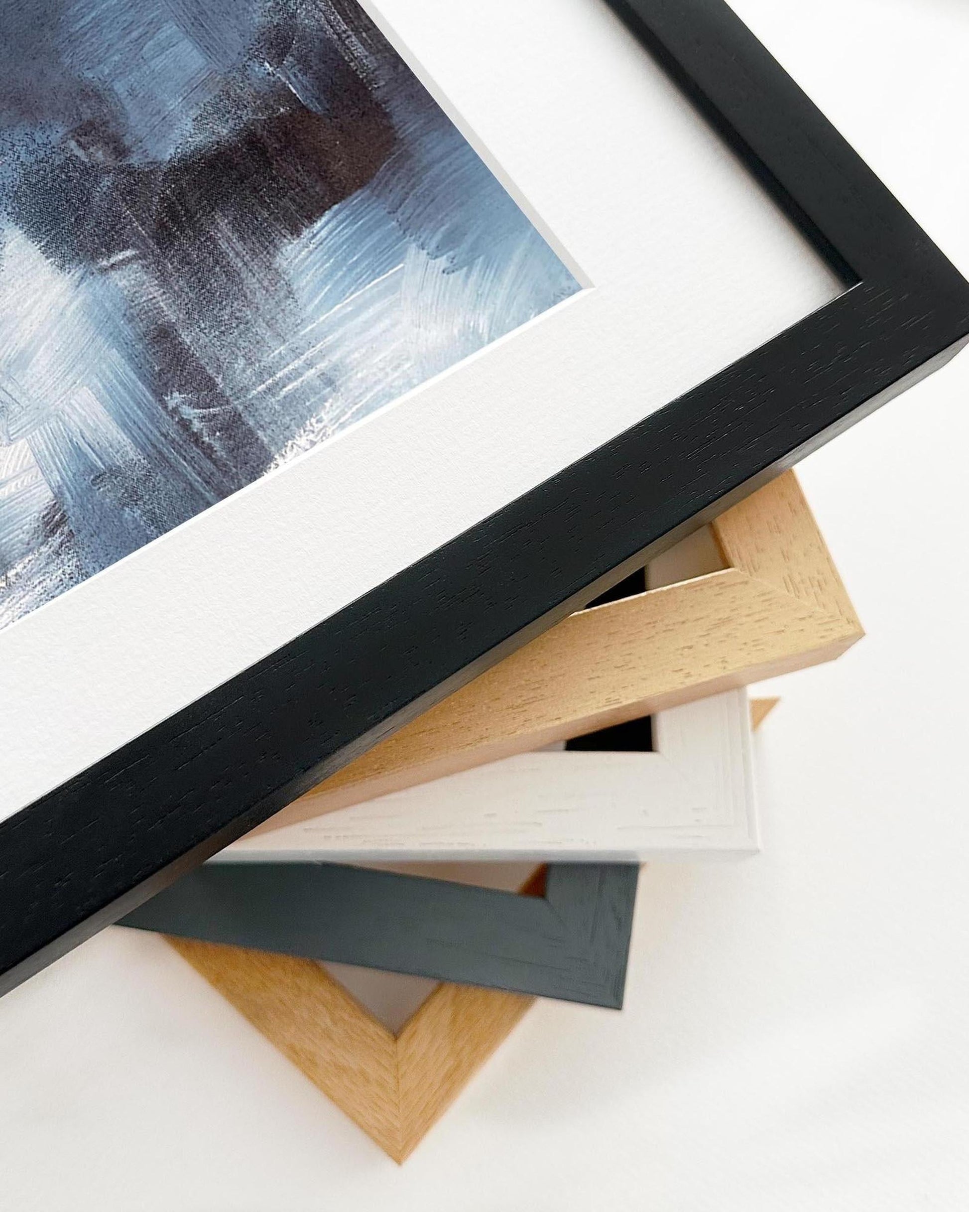 Close-up of various picture frames on a white surface with a painting in the background.
