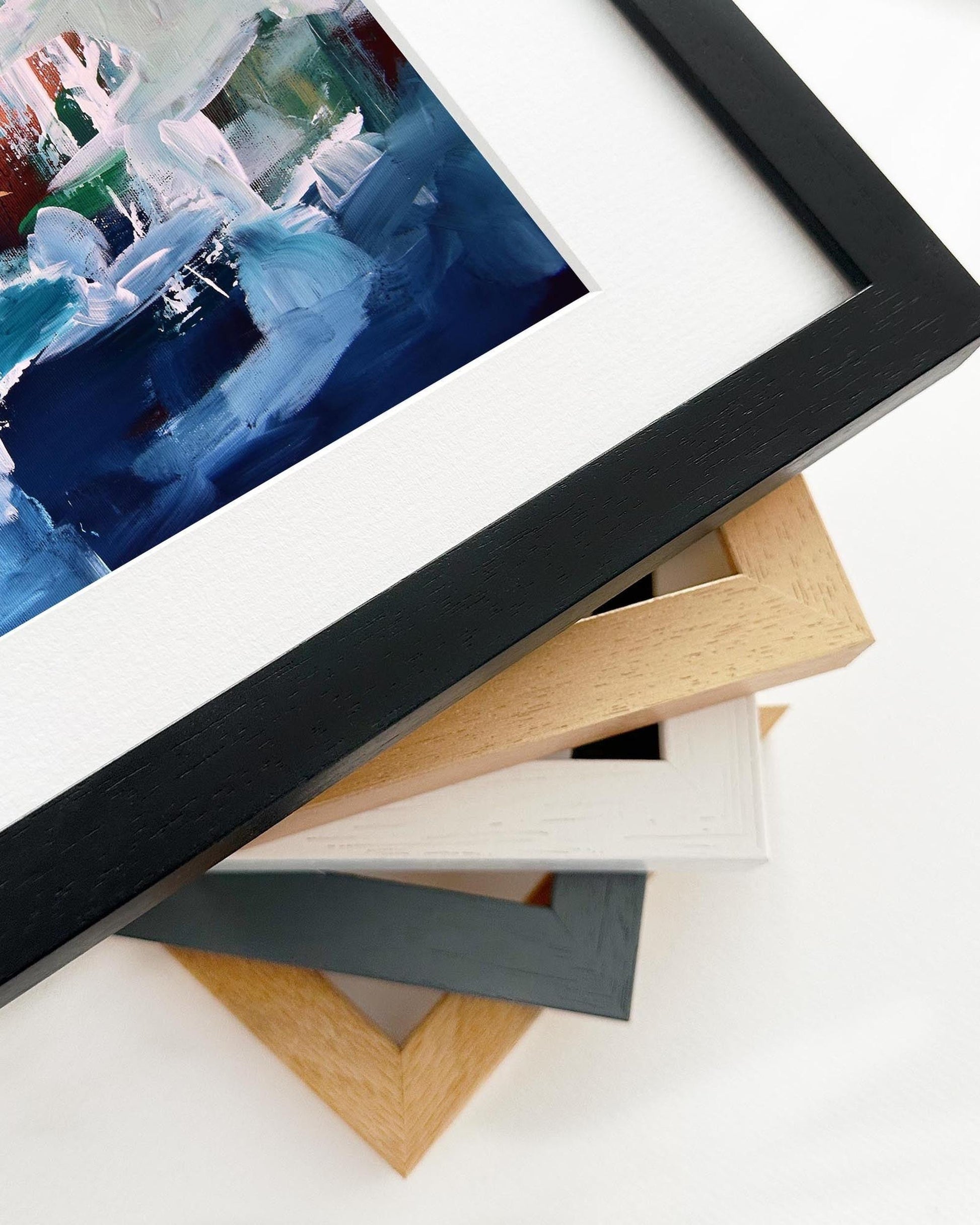 Close-up of a framed artwork with various wooden picture frames on a white surface.