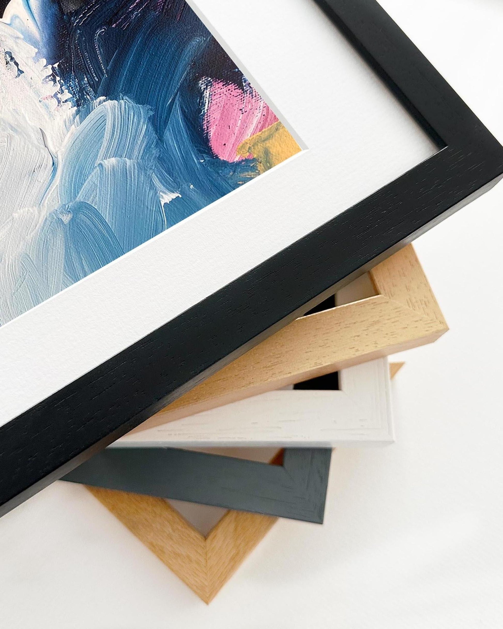 Collection of various picture frames on a white surface with a painting in the background.