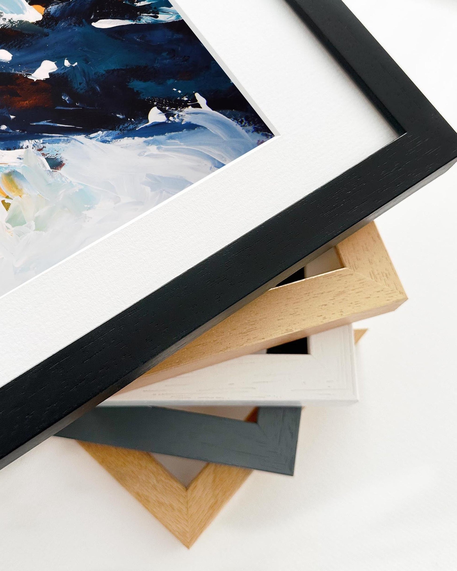 Close-up of a framed painting with various frame options on a white surface