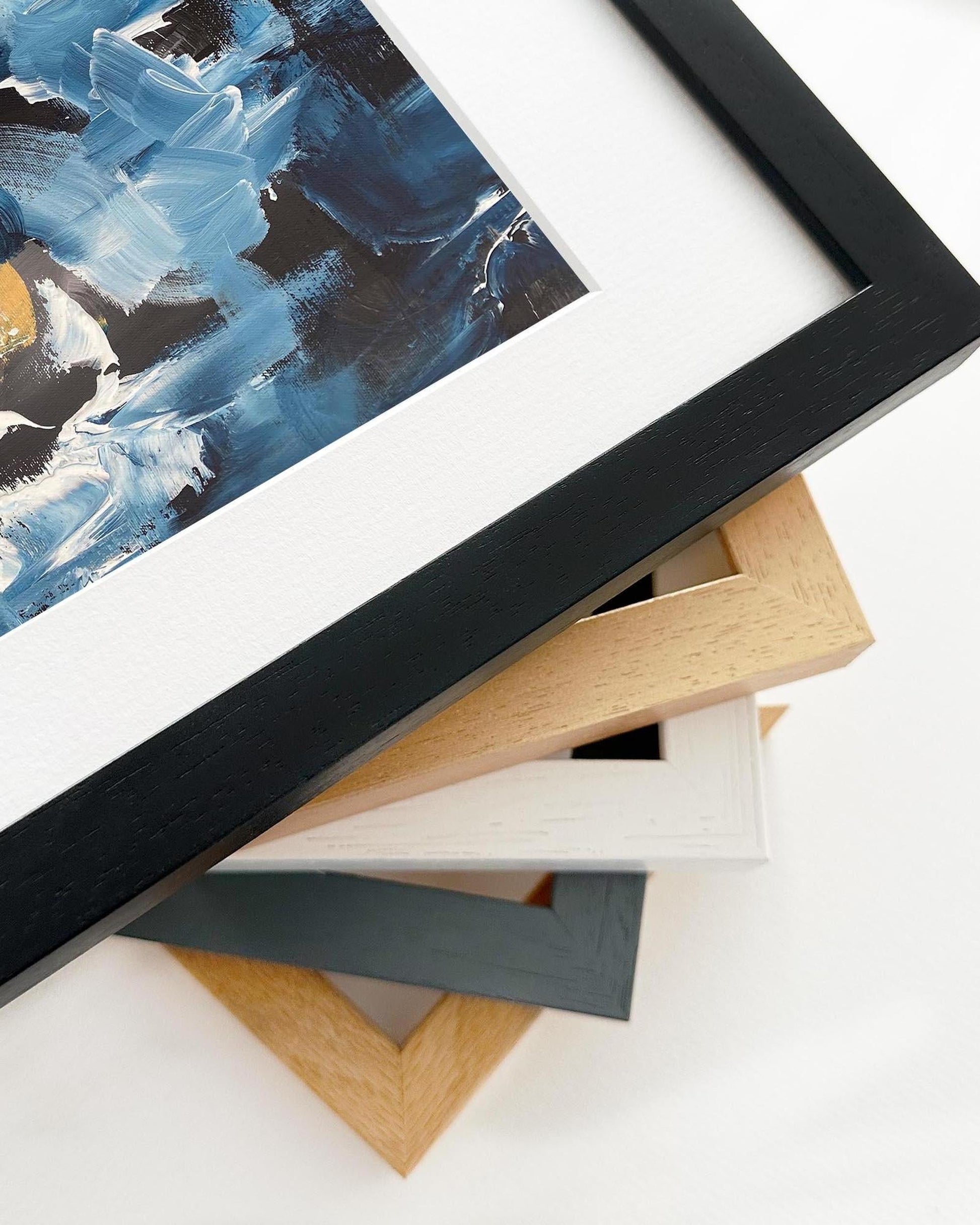 Close-up of a framed abstract painting with various wooden picture frames on a white surface.
