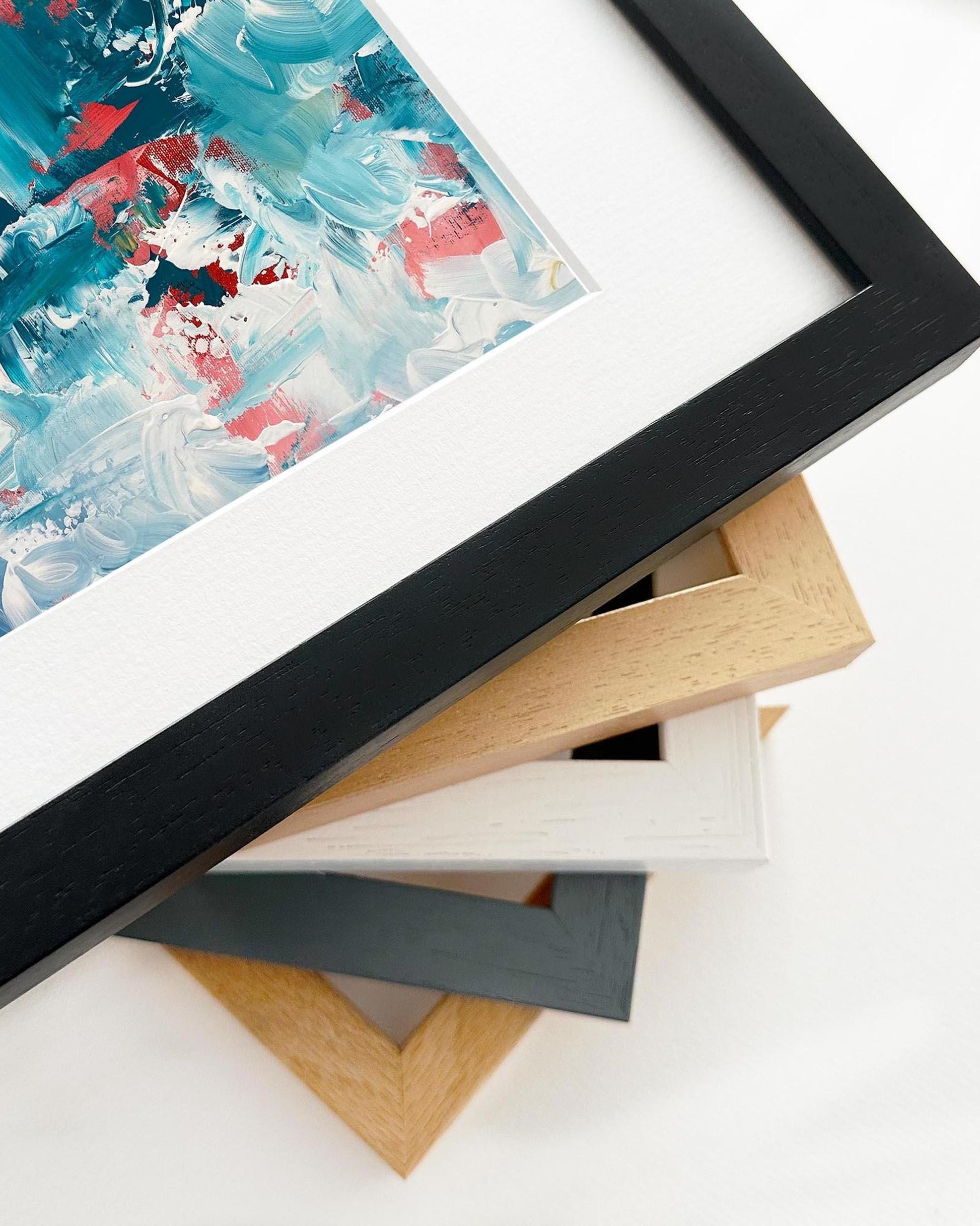 Framed abstract artwork with a stack of variously colored frames on a white surface.