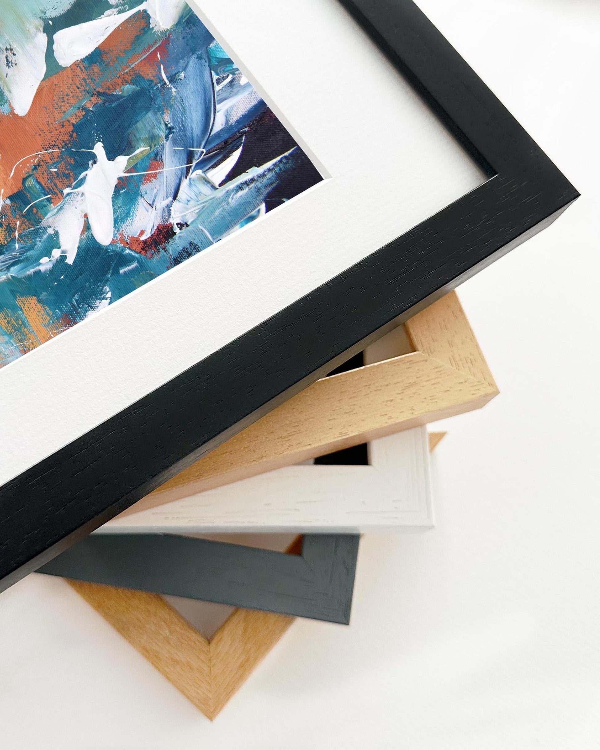 Stack of variously framed artworks on a white surface