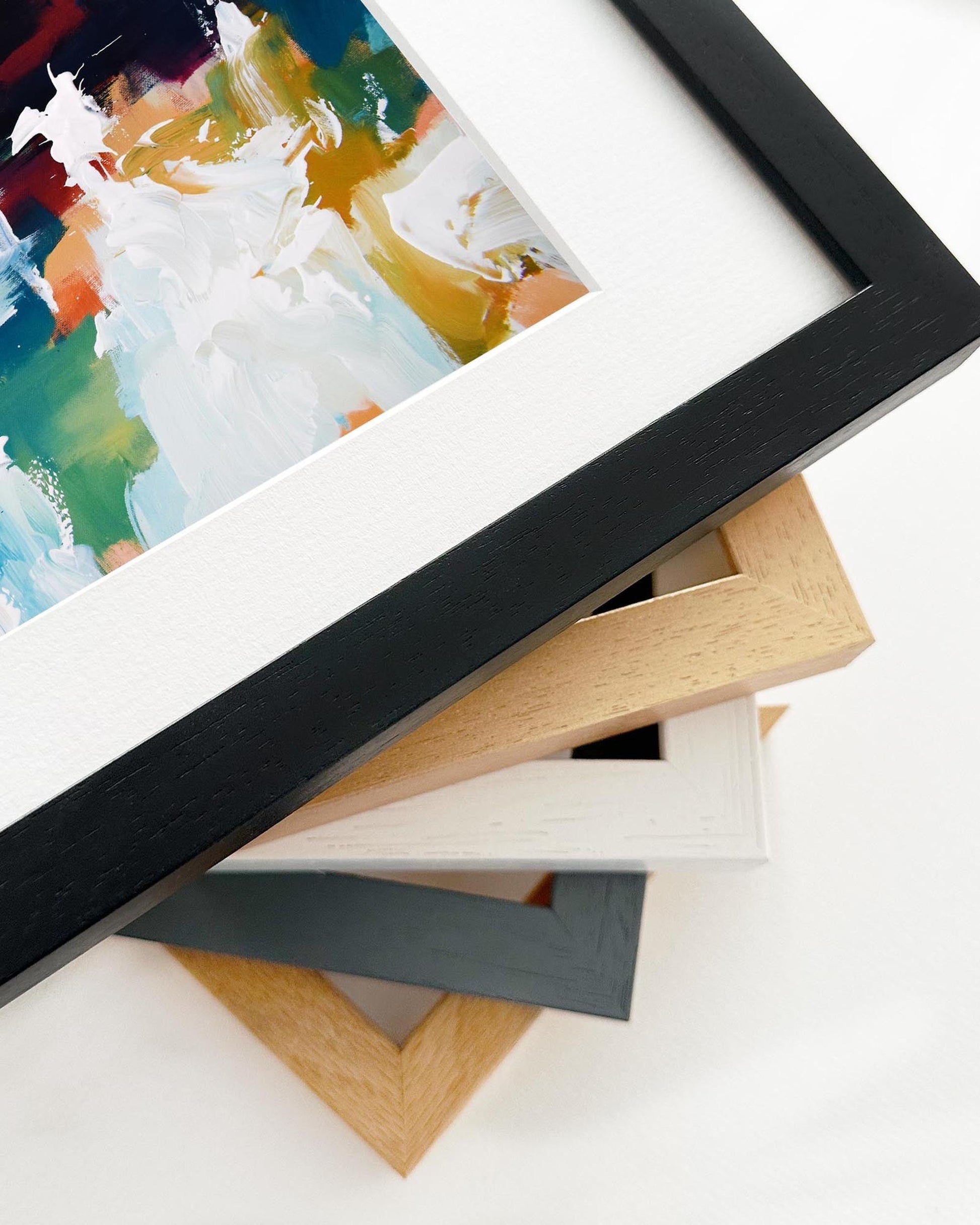 Collection of picture frames in various colors on a white surface with a colorful painting in the background.