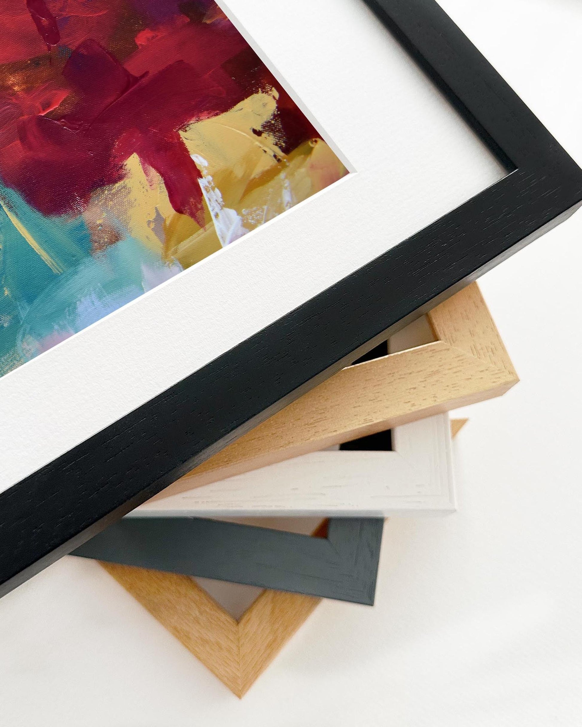 Collection of variously colored picture frames on a white surface with a framed abstract painting in the background.