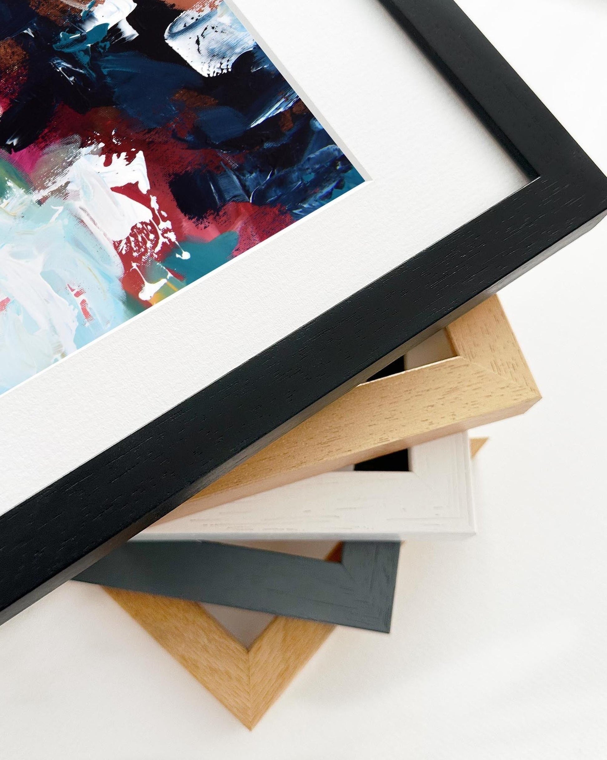 Close-up of various picture frames on a white surface with a colorful painting in the background.