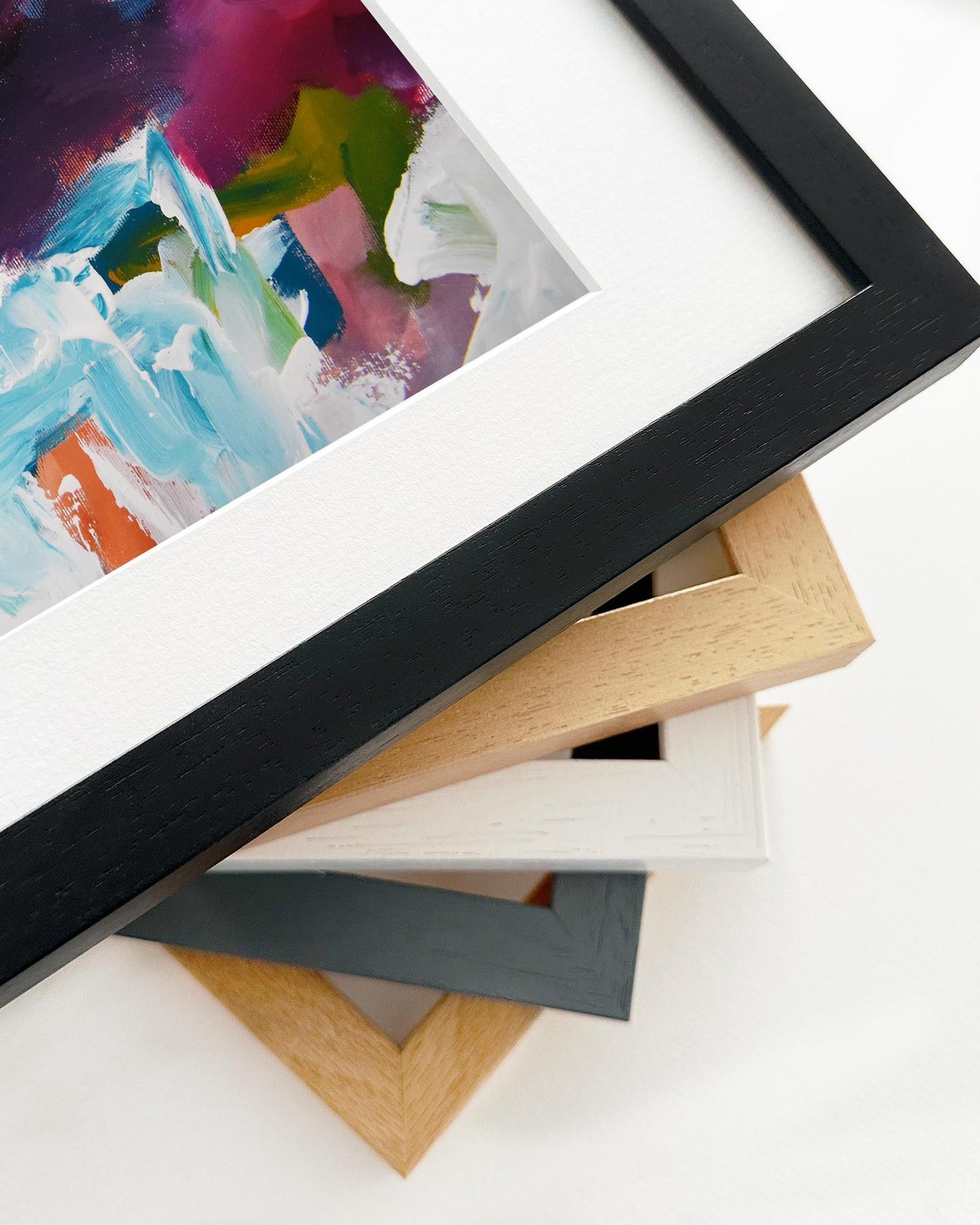 Stack of various picture frames on a white surface with a colorful abstract painting in the background.