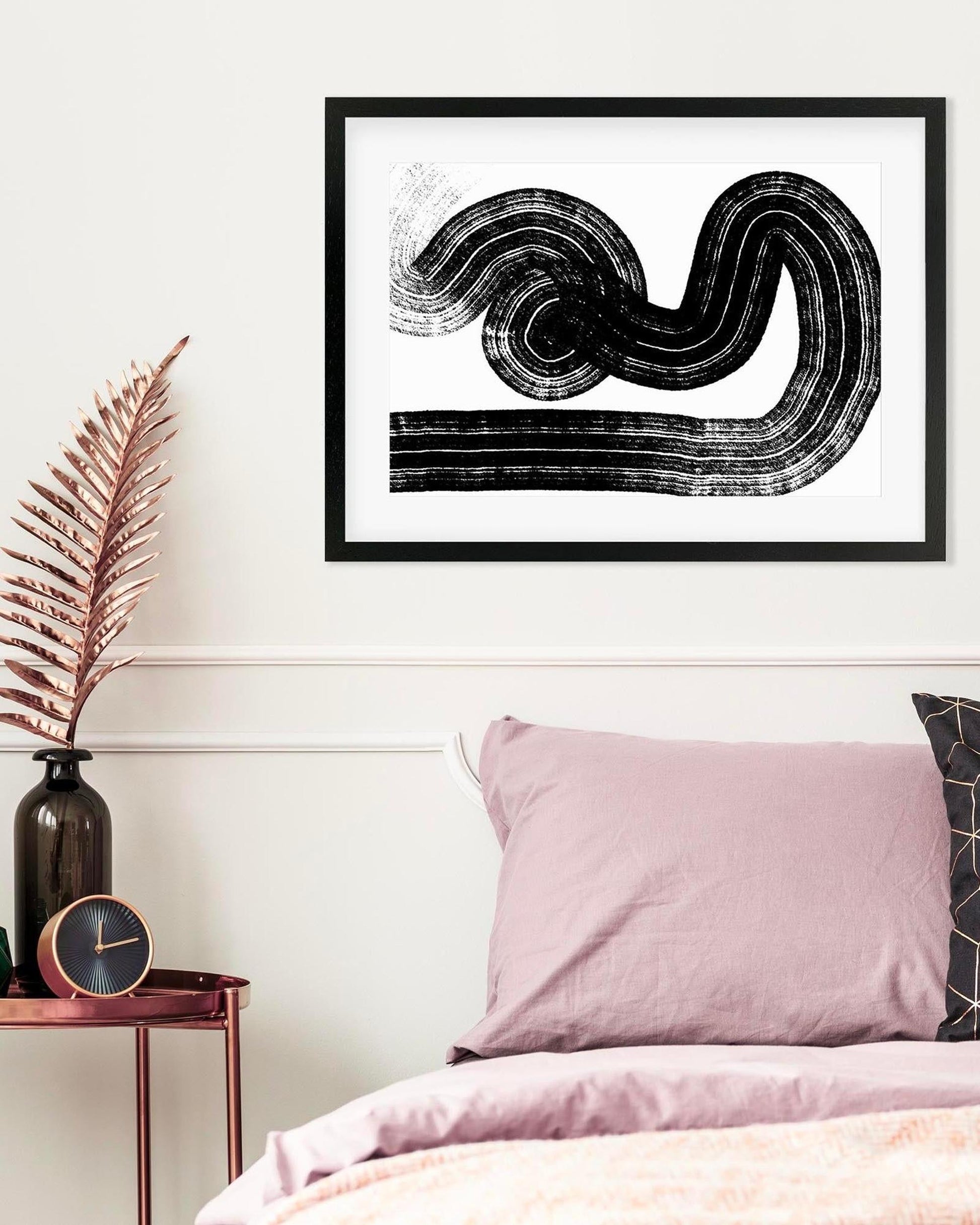 Framed abstract art print on a wall above a bed with pink bedding.