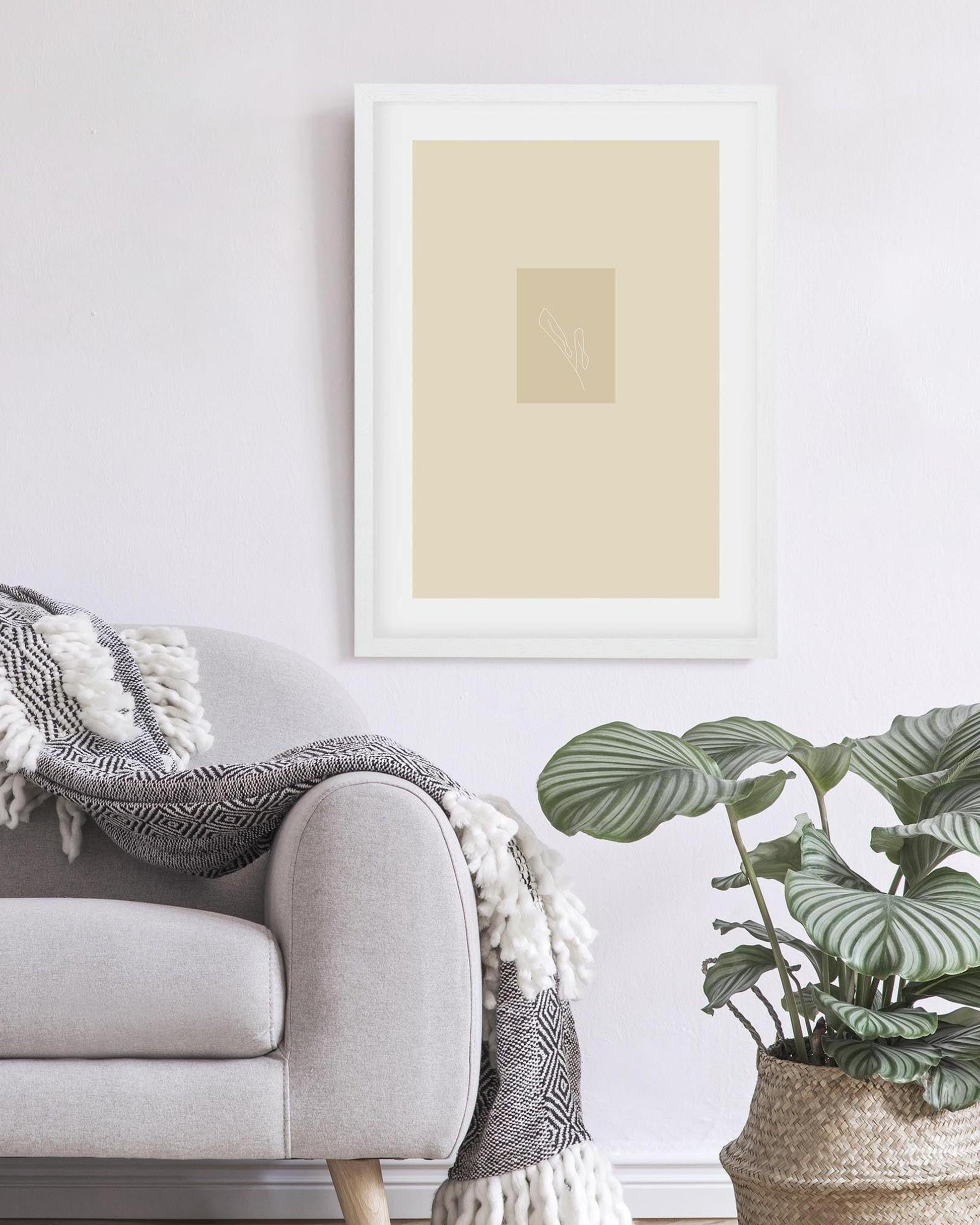 Framed abstract art piece on a wall above a sofa with a plant in the foreground
