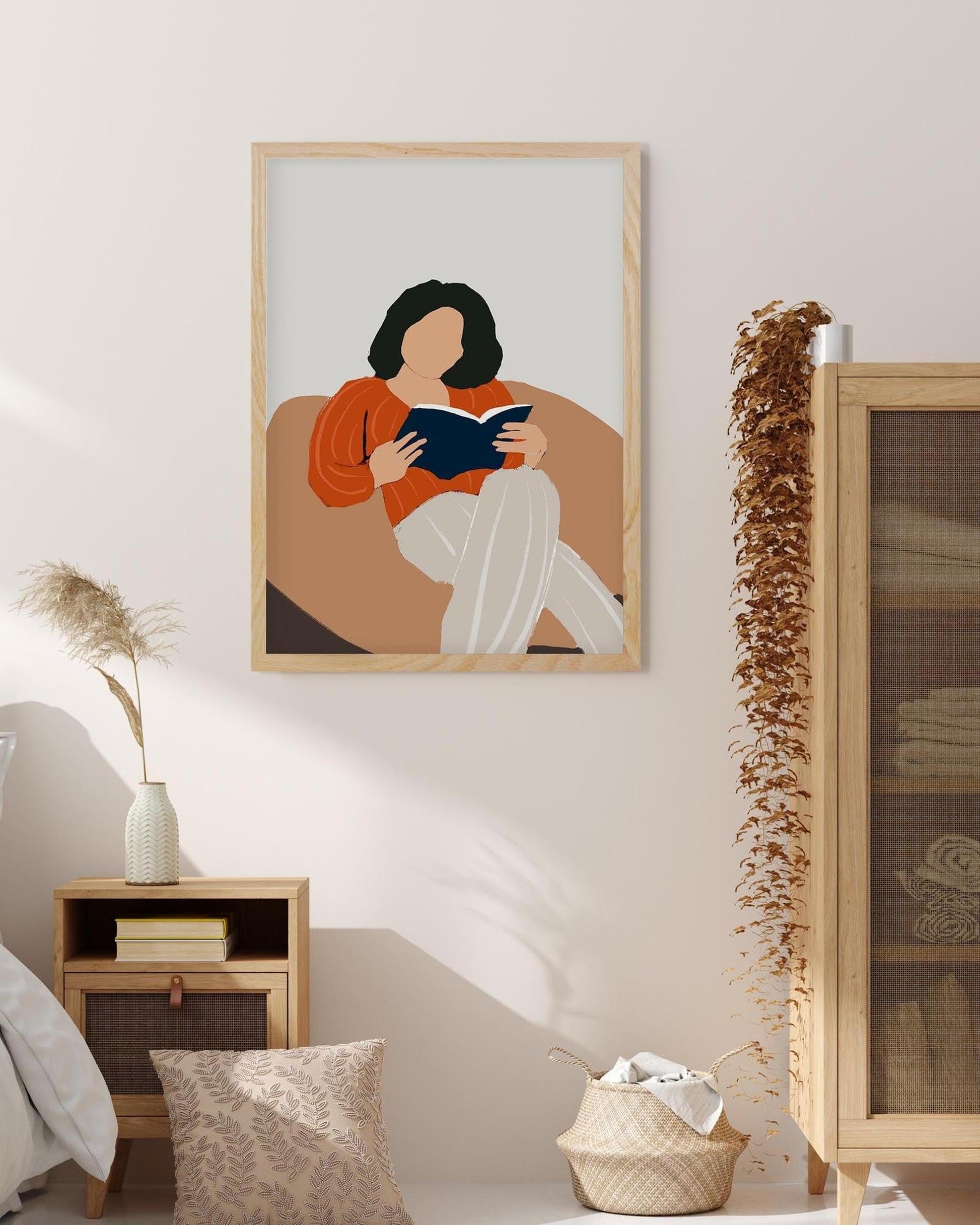 Framed artwork of a woman reading a book on a wall in a room with decor elements.