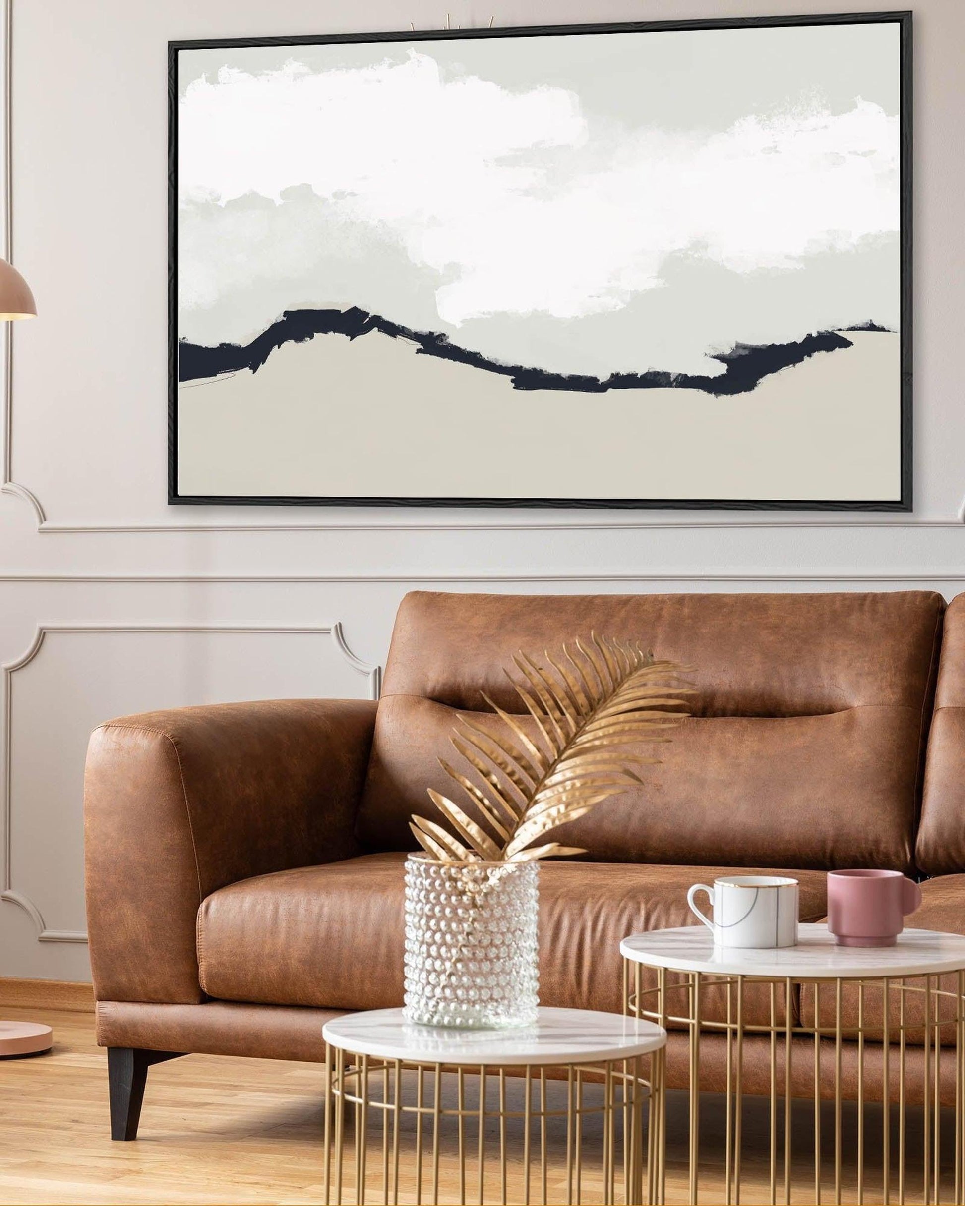 Living room with a brown leather sofa, gold coffee table, and abstract wall art.