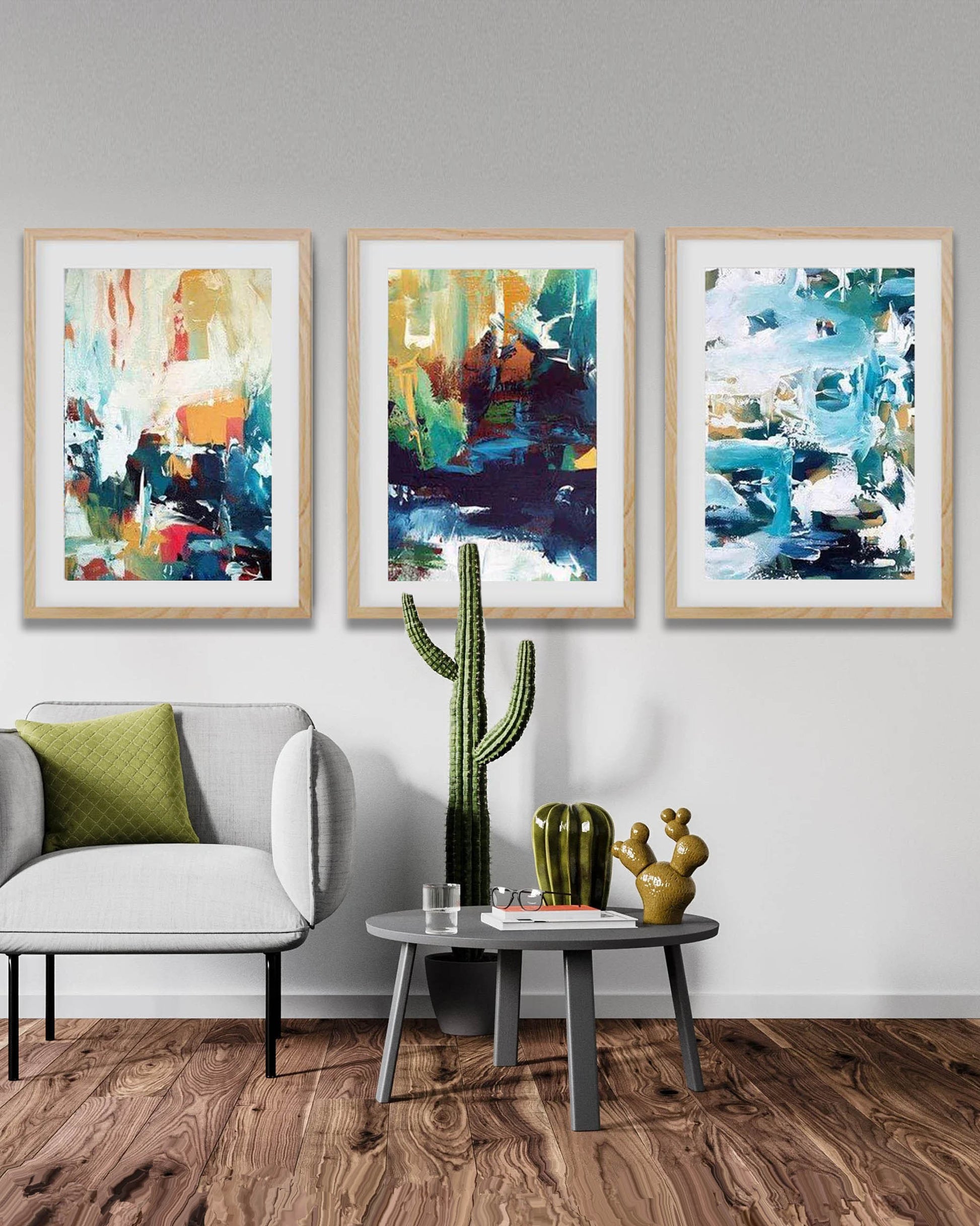 Three abstract paintings on a wall above a grey sofa with decorative plants. Colourful modern home decor in bohemian stylish living room.