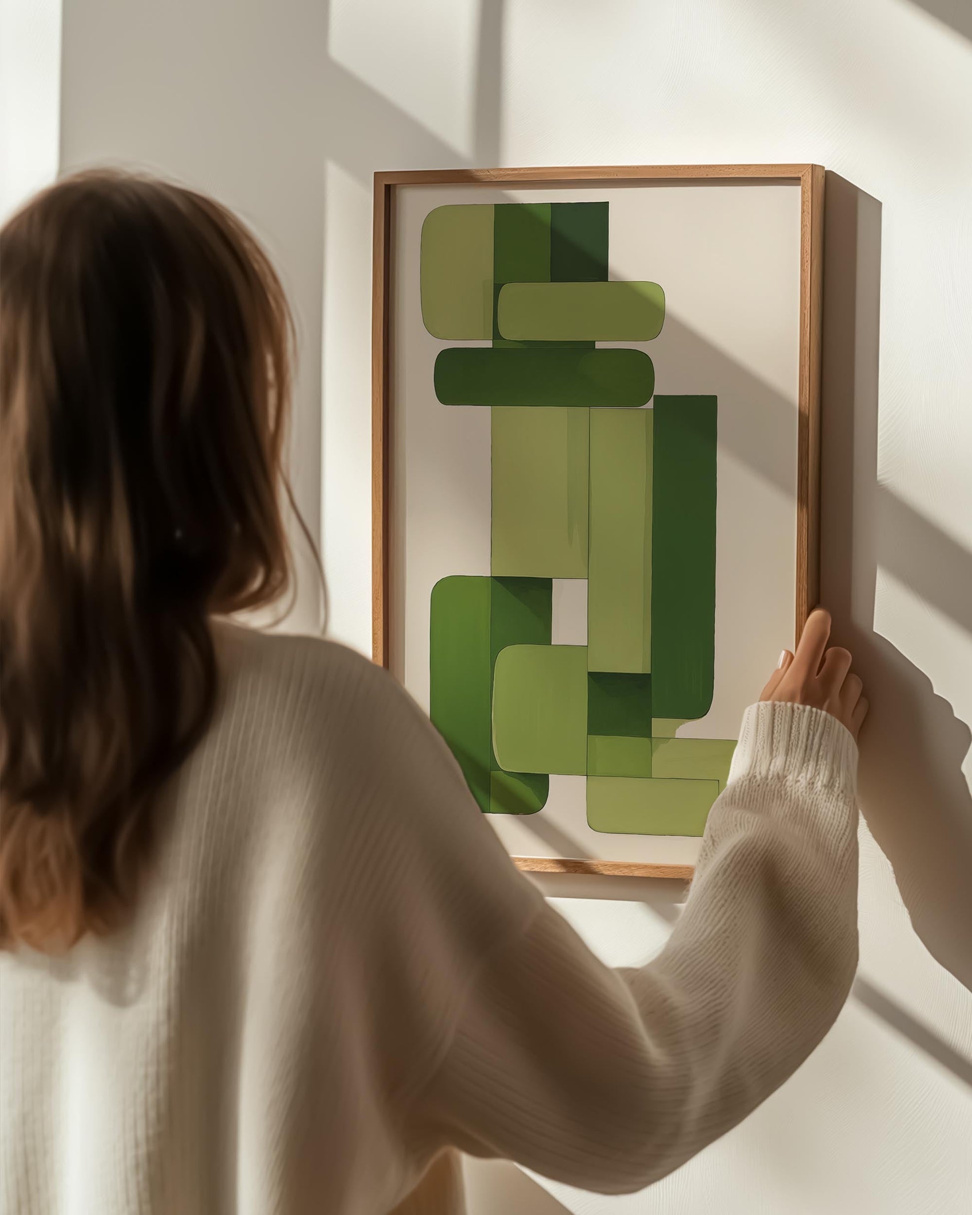 Person hanging a framed abstract green art piece on a wall