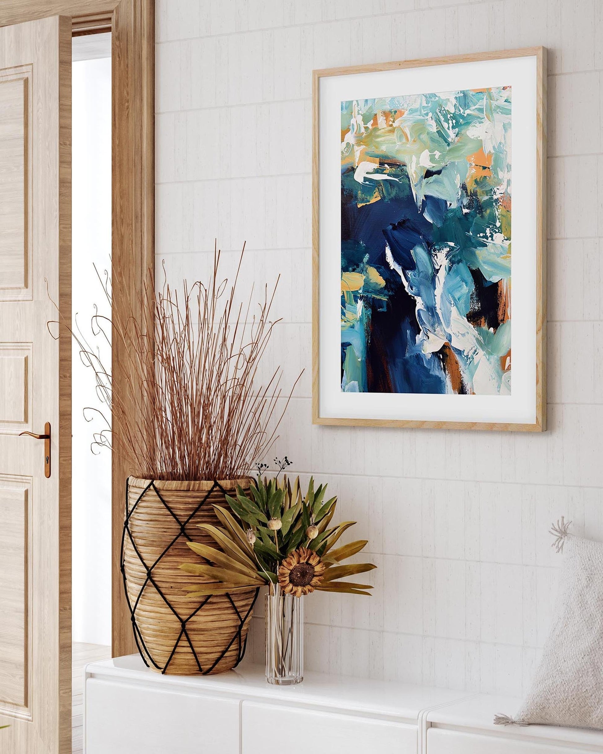 Framed abstract art on a wall with decorative plants and a open door.