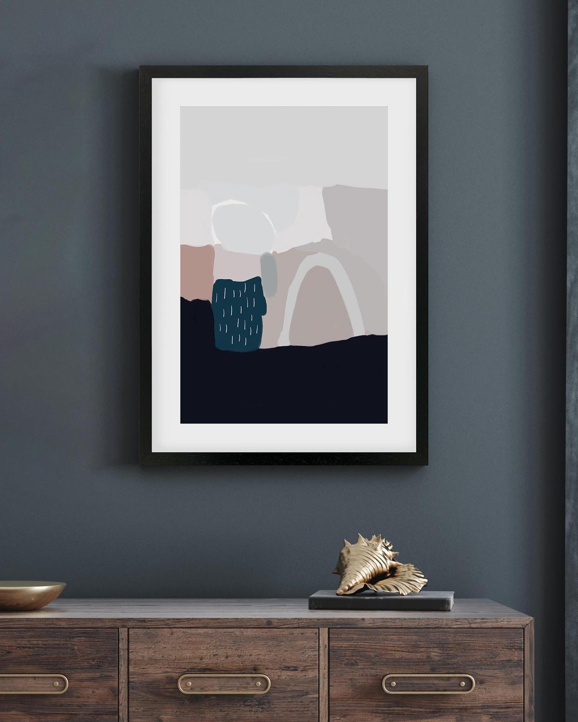 Framed abstract art piece on a dark gray wall above a wooden cabinet.